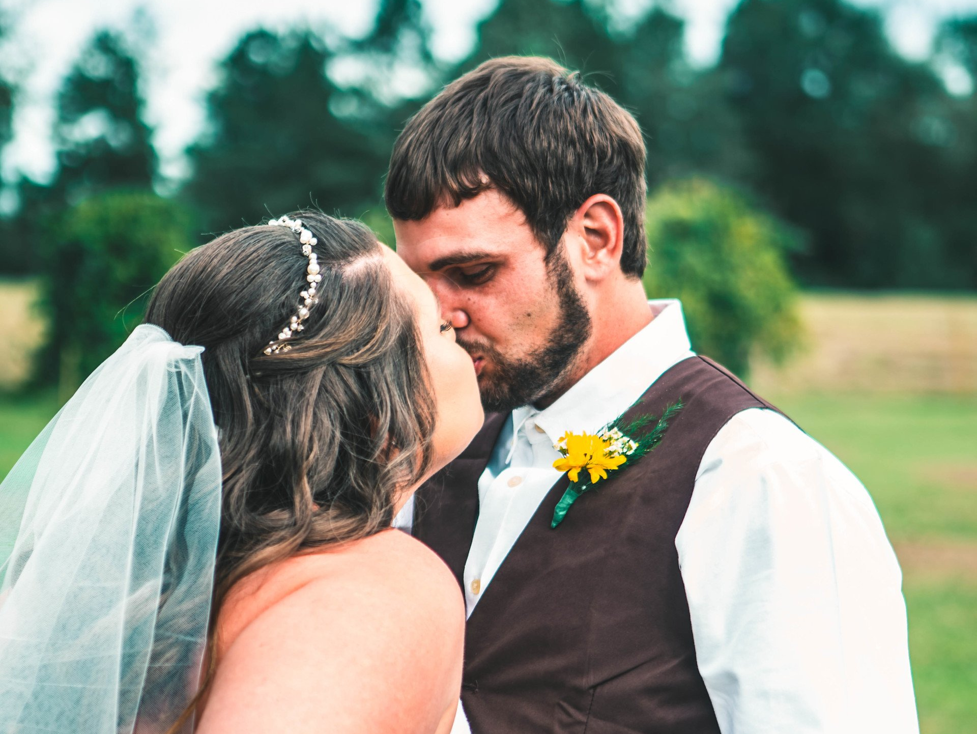 A bride and groom kissing in a field with trees in the background