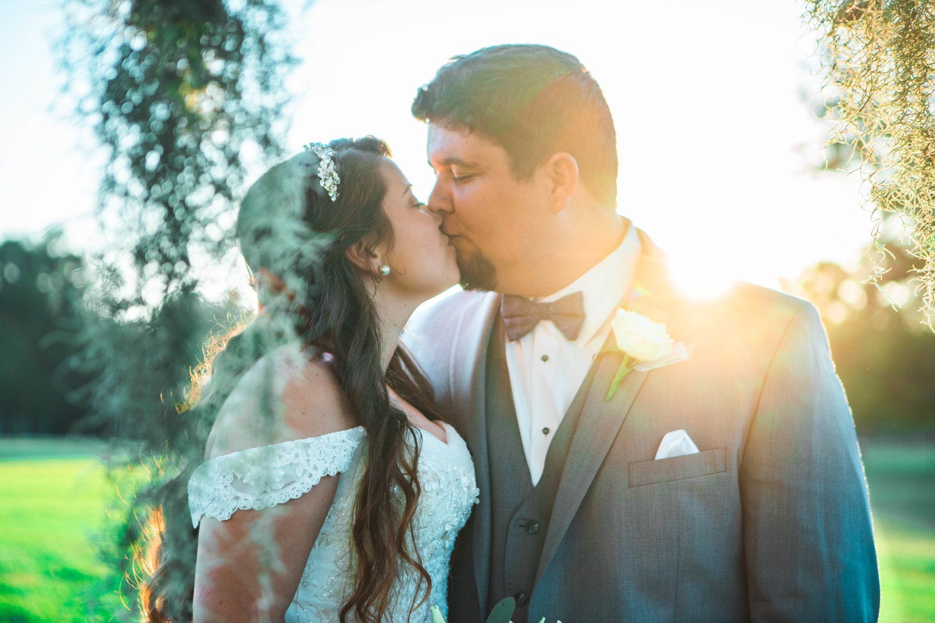 A bride and groom are kissing in front of a tree.
