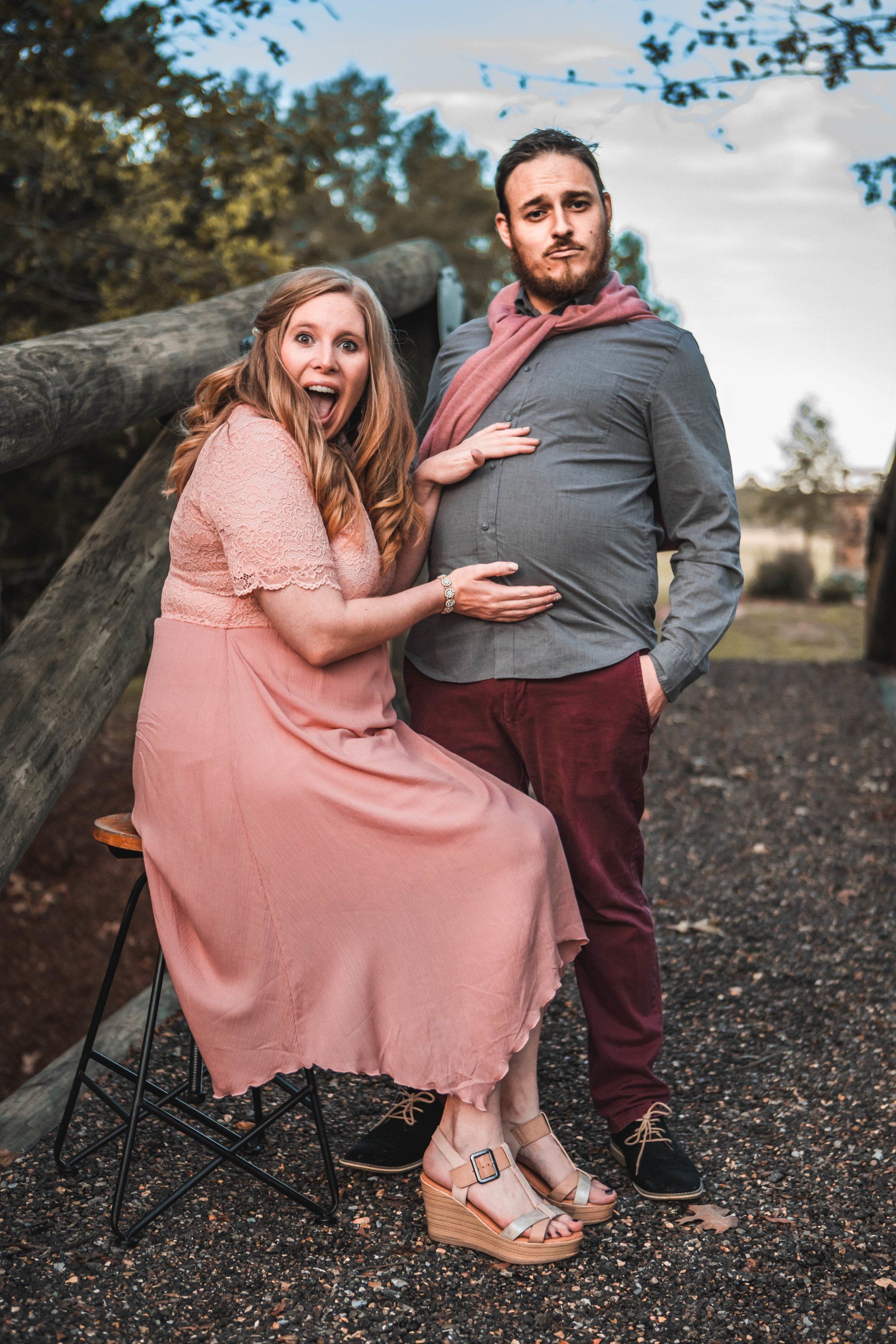 A man and a woman are posing for a picture while the woman is sitting on a stool.