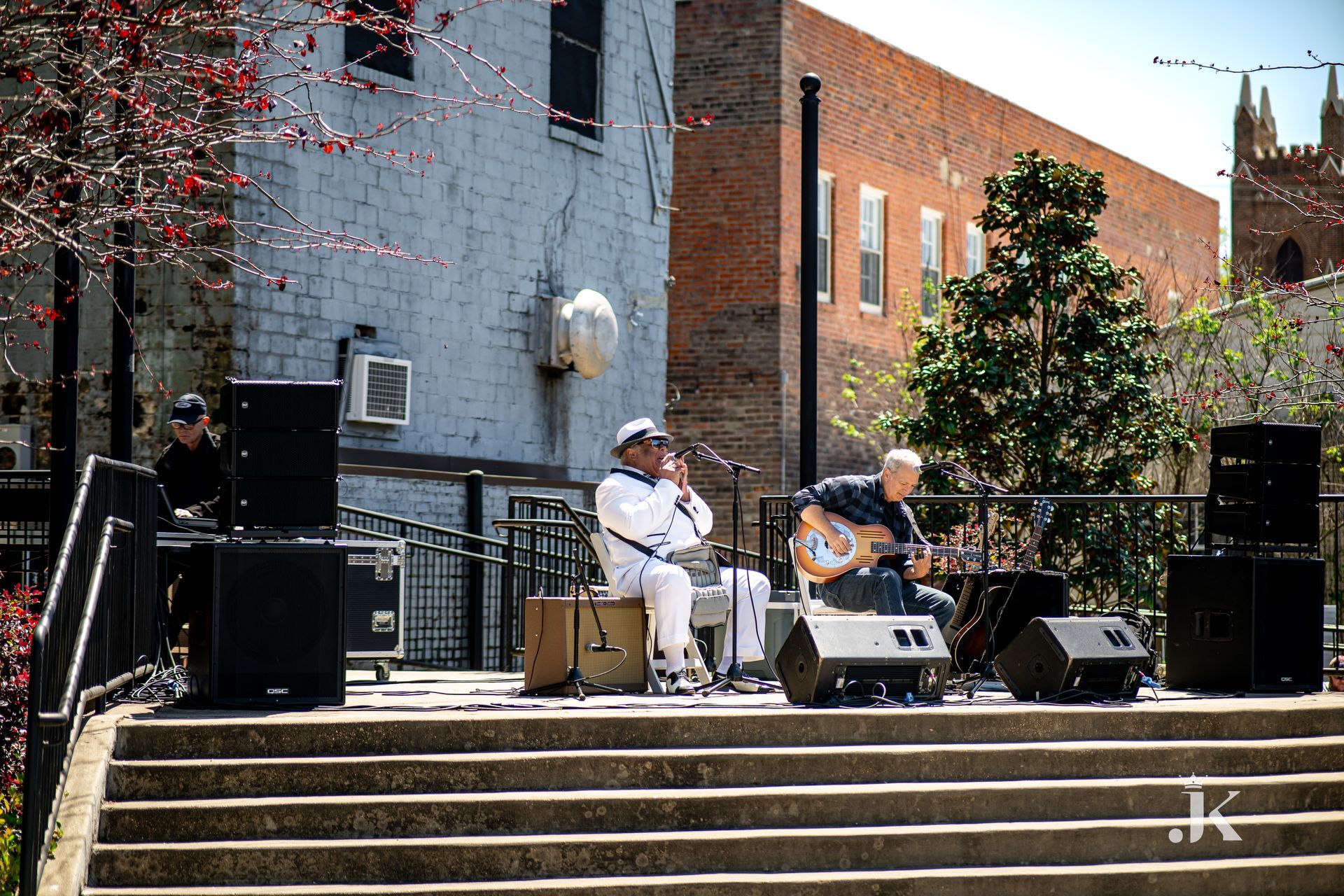 Two men are playing instruments on a stage in front of a building.