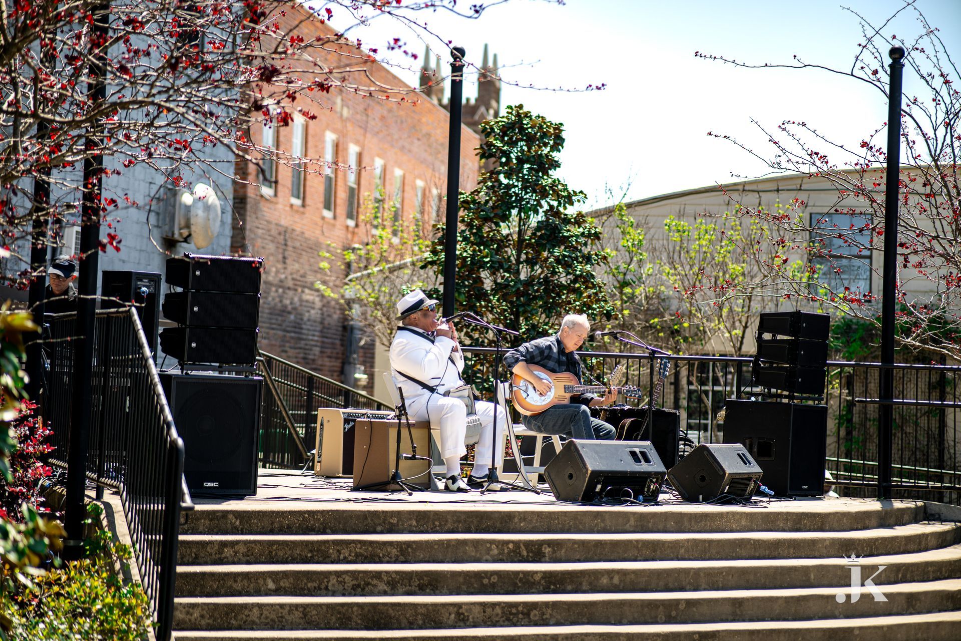 Two men are playing instruments on a stage in front of a building.