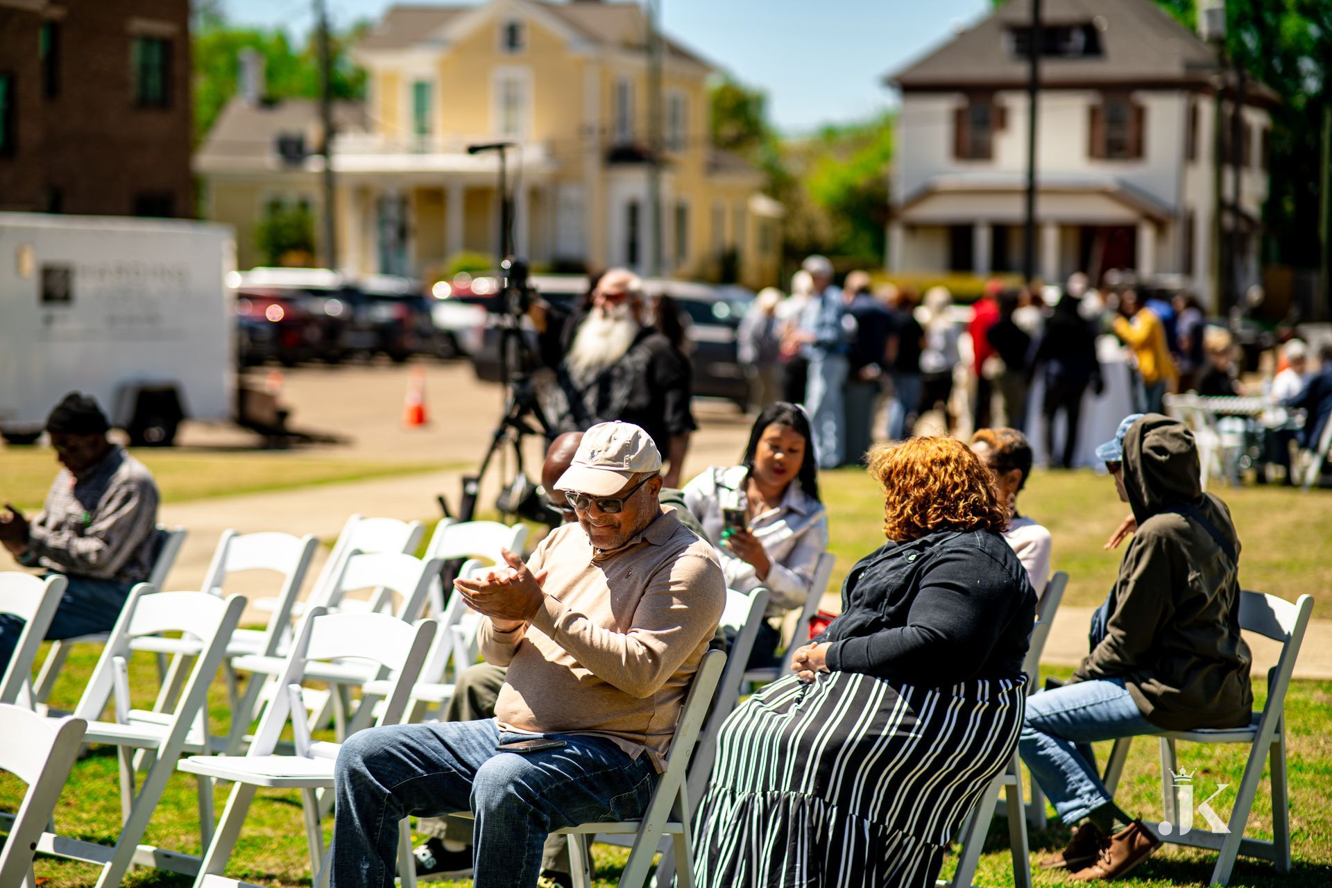 A group of people are sitting in white folding chairs in a park.