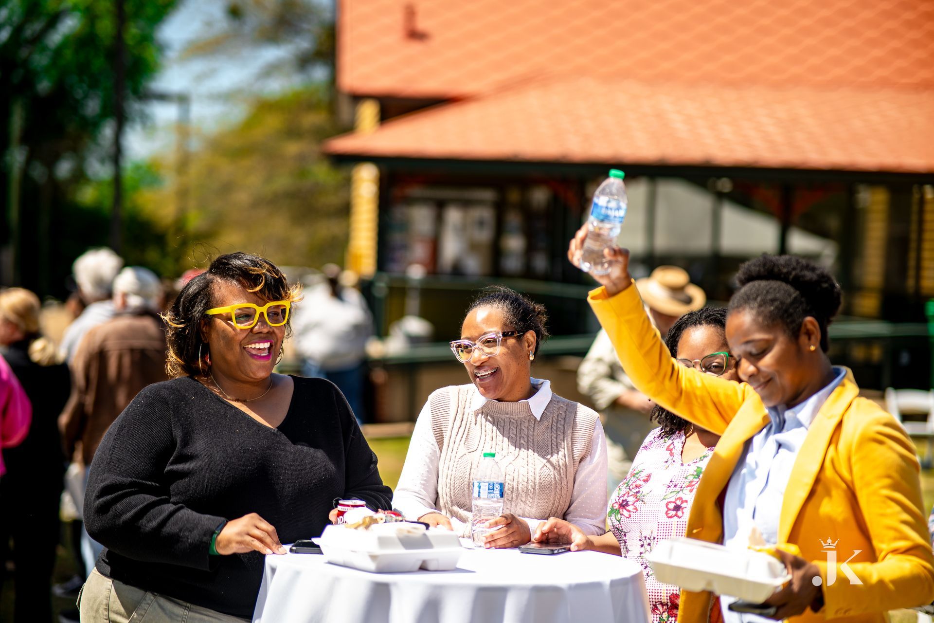 A group of women are standing around a table with a woman holding a bottle of water.