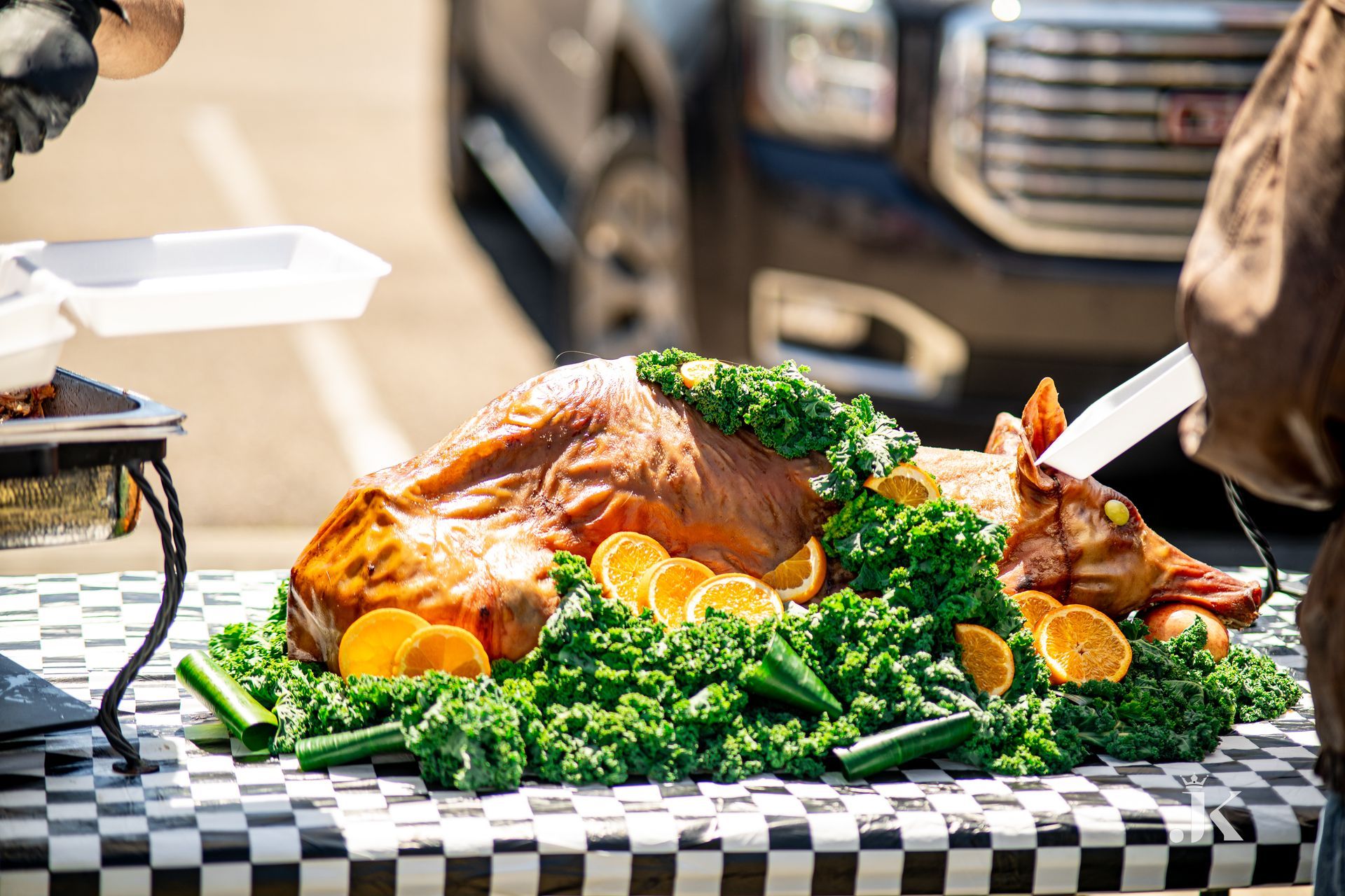 A roasted pig is sitting on a checkered table with vegetables.