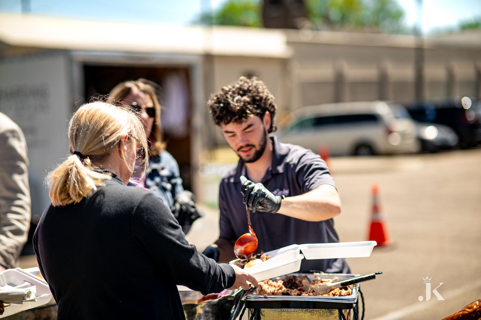 A man is serving food to a woman in a parking lot.