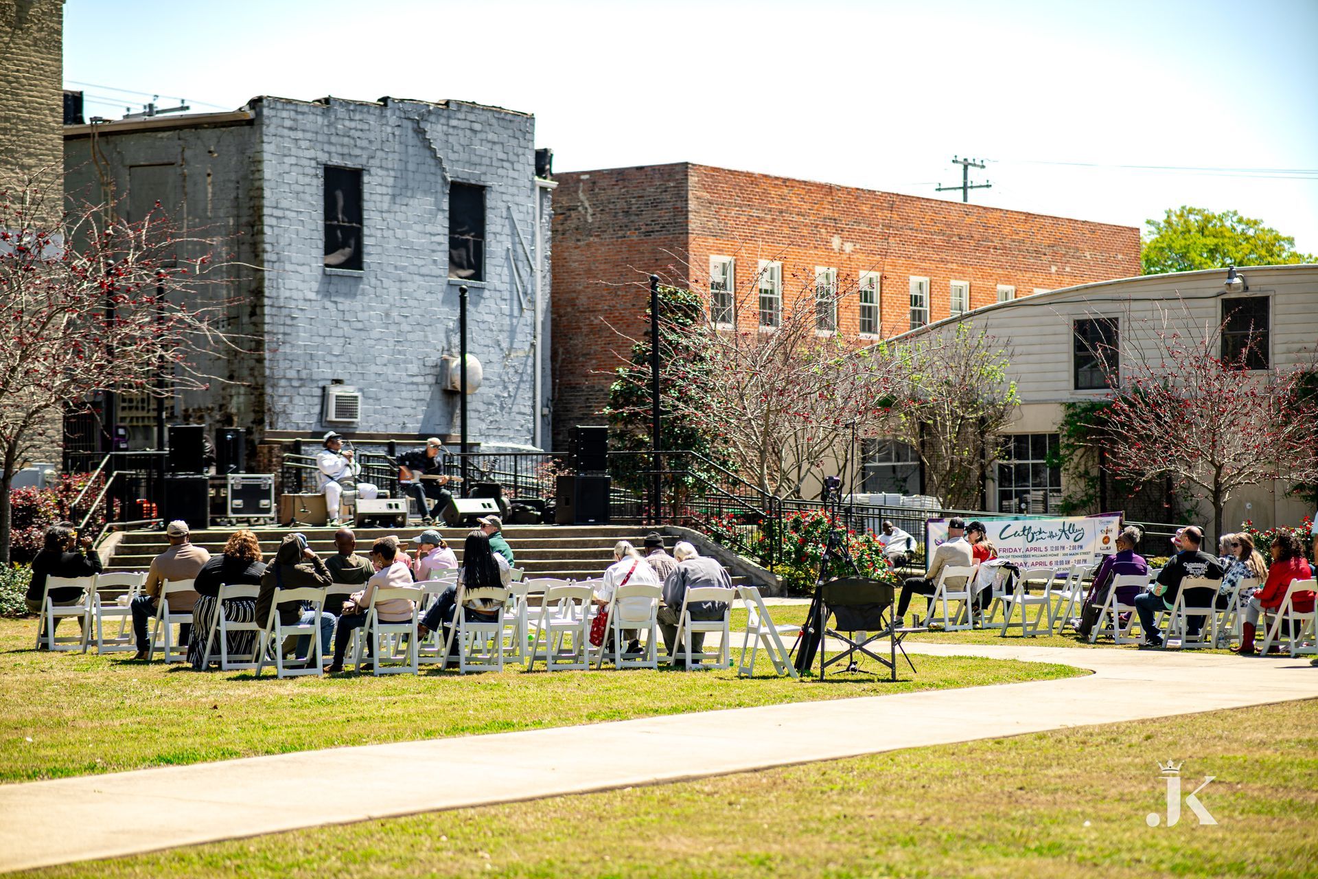 A group of people are sitting at tables in a park in front of a building.