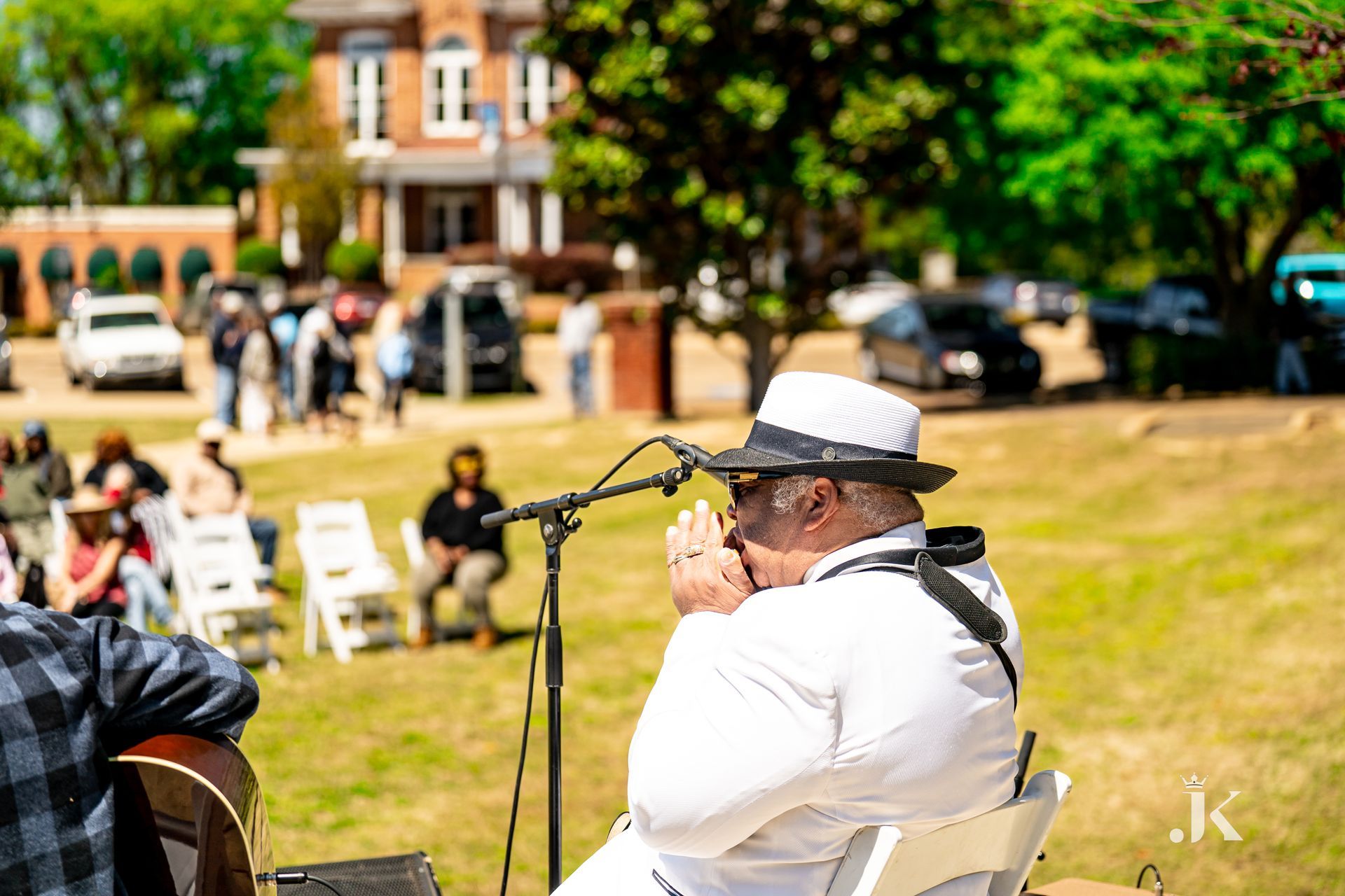 A man is playing a harmonica in front of a microphone in a park.