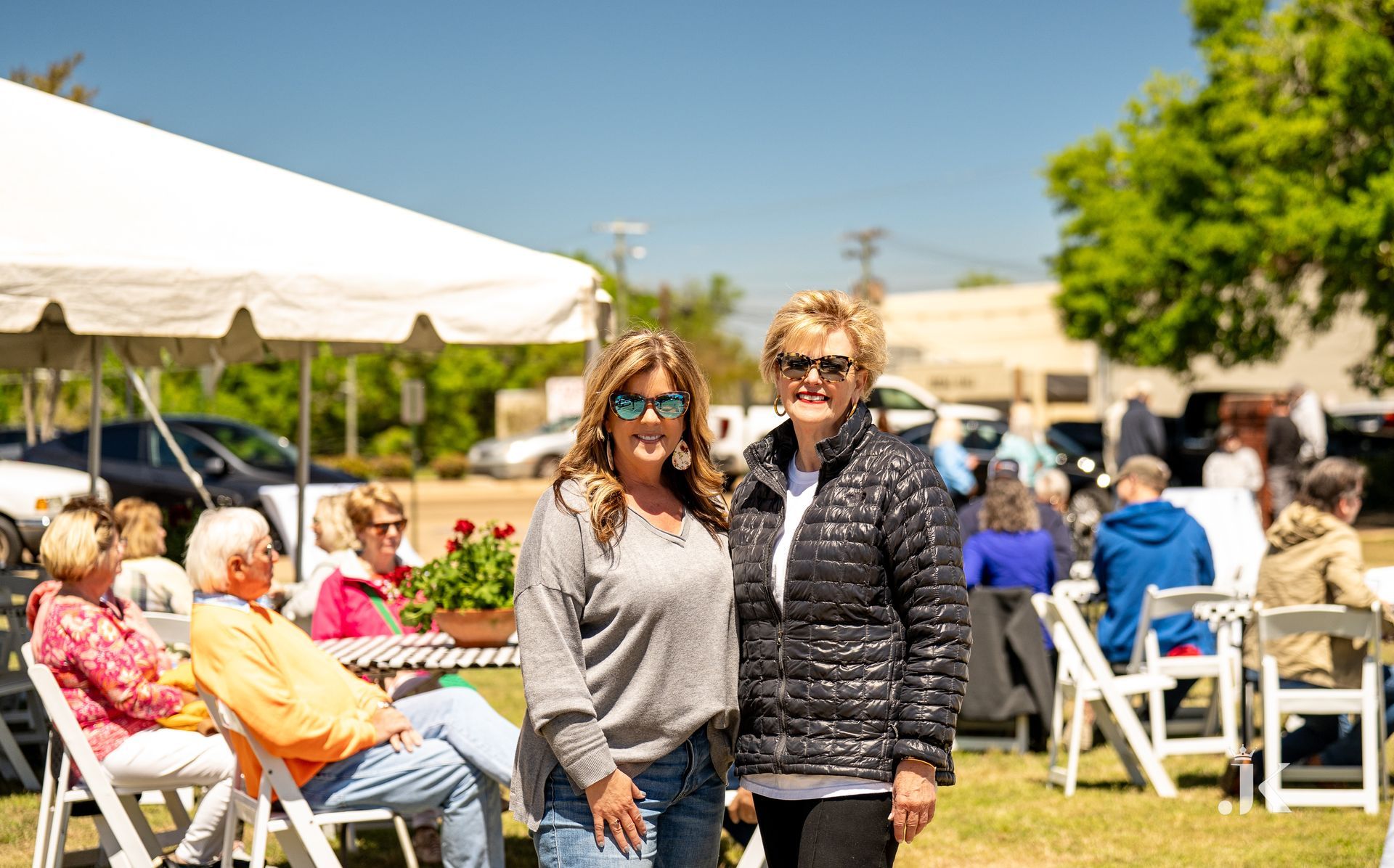 Two women are standing next to each other in front of a crowd at a picnic.