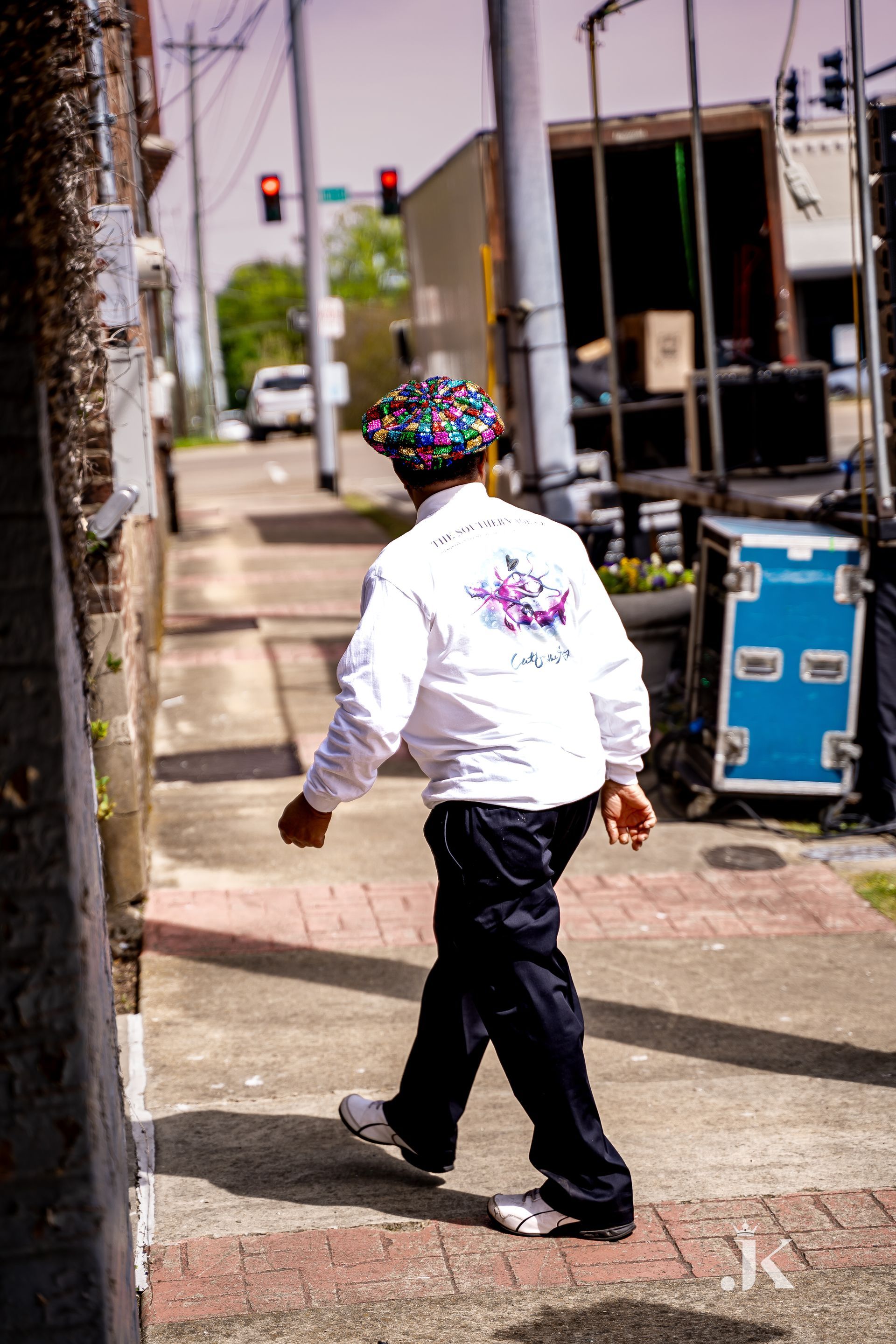 A man wearing a hat and a white shirt is walking down a sidewalk.