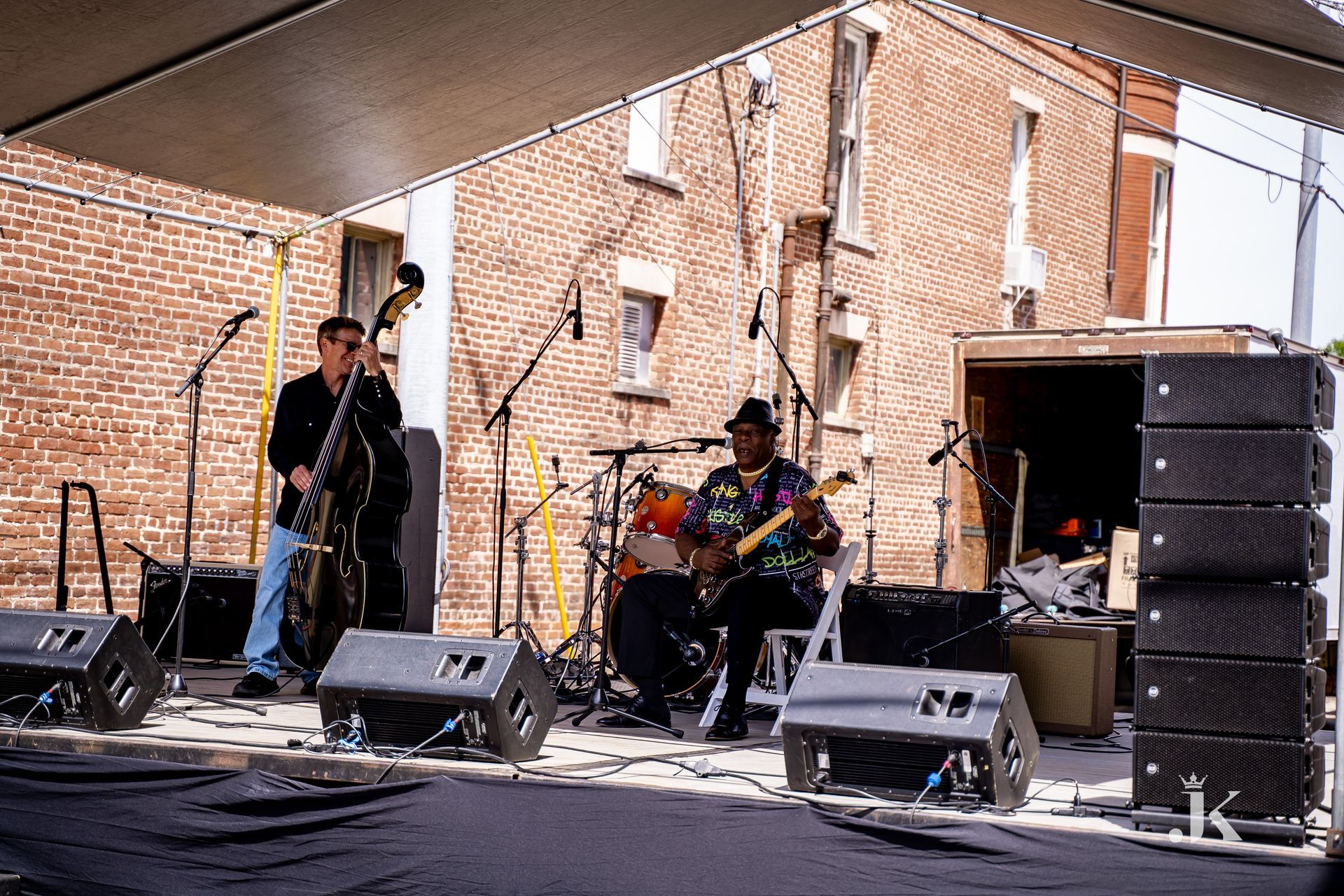 Two men are playing instruments on a stage in front of a brick building.