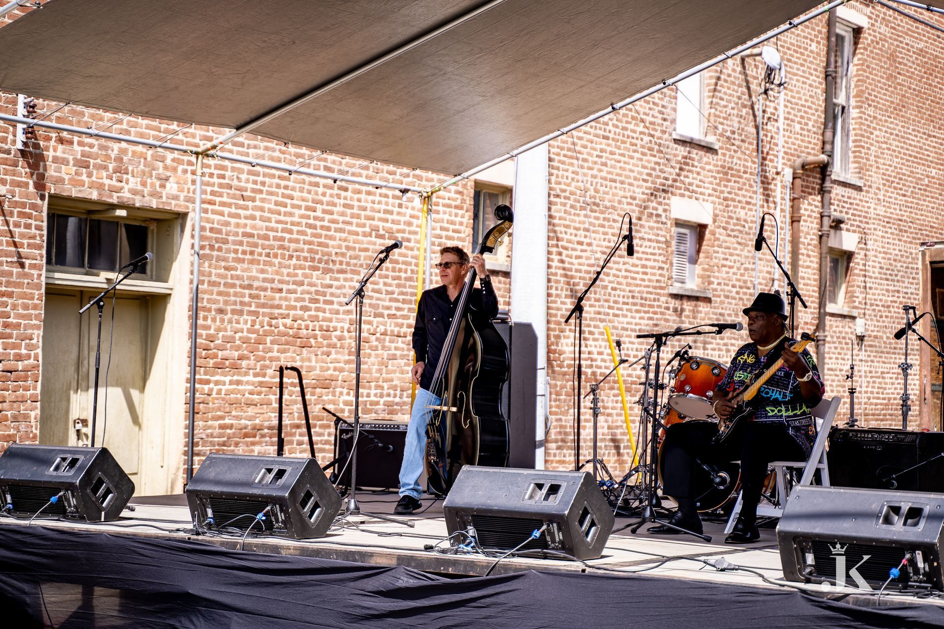Two men are playing instruments on a stage in front of a brick building.