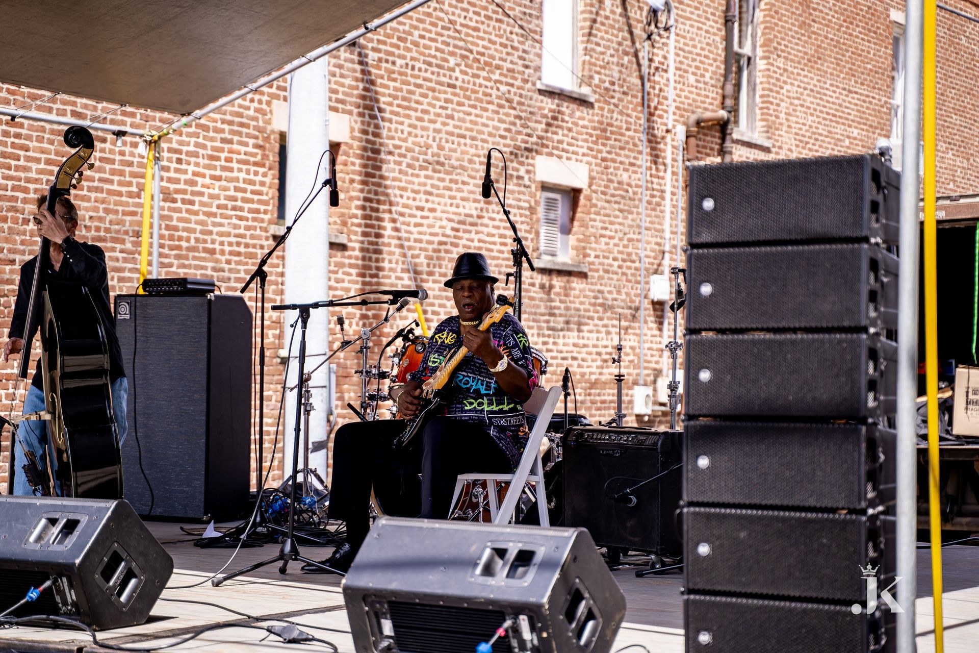 A man is playing a guitar on a stage in front of a brick building.