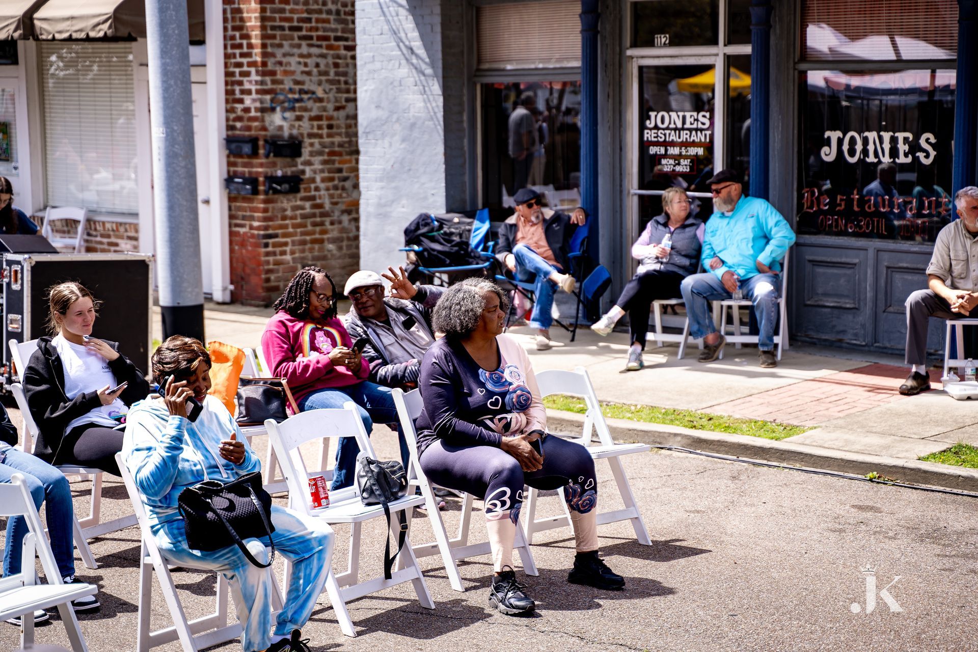 A group of people are sitting in chairs on the sidewalk in front of a store.