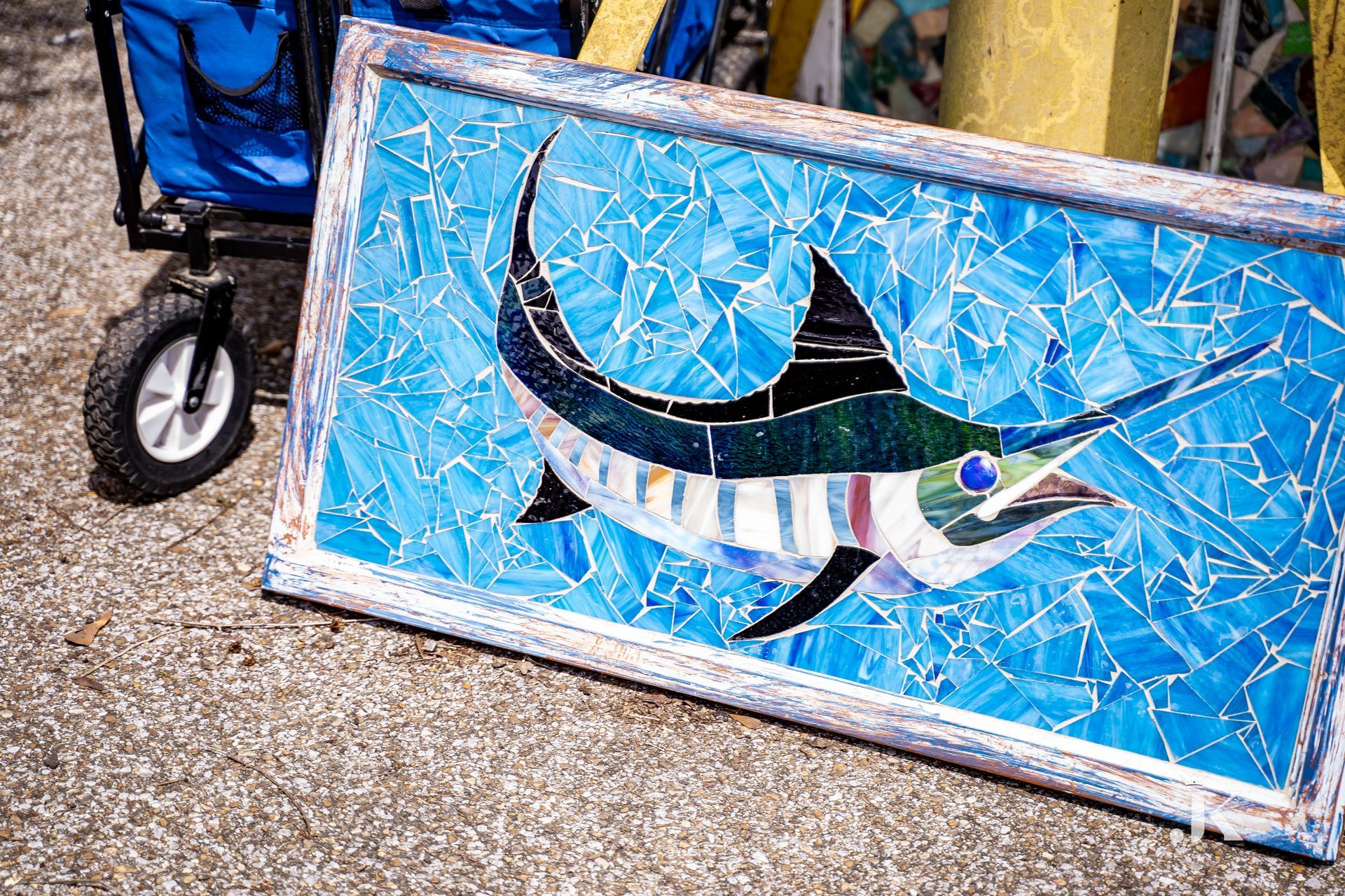A painting of a marlin is sitting on the ground next to a wagon.