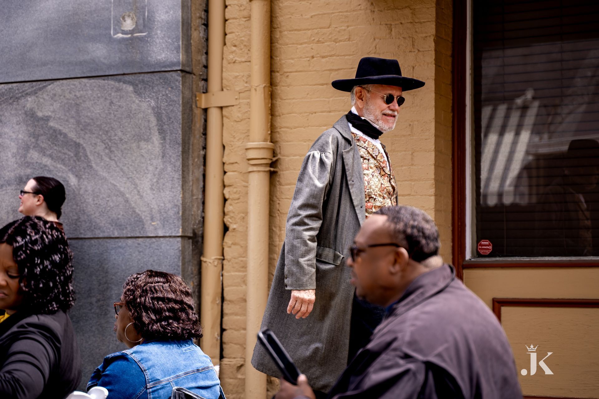A man wearing a hat and sunglasses is walking down the street