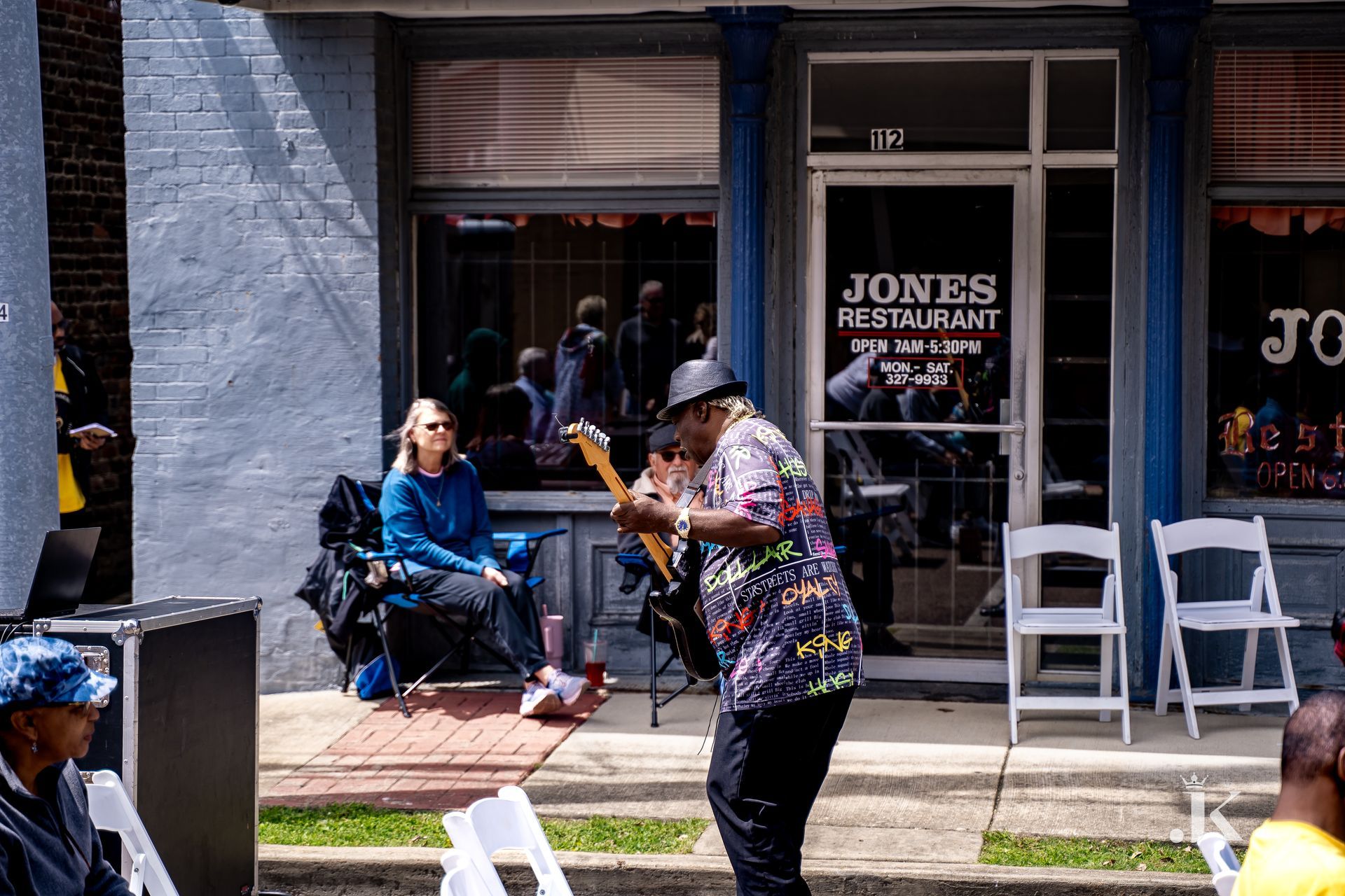 A man is playing a guitar in front of a restaurant called jones restaurant.