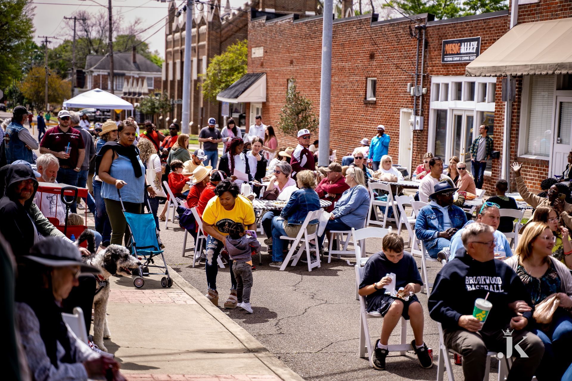 A crowd of people are sitting at tables and chairs on the sidewalk.