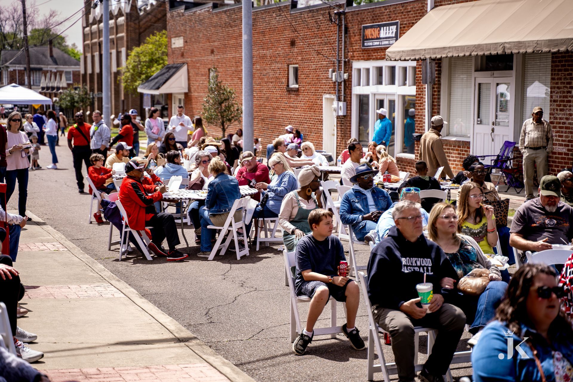 A large group of people are sitting at tables and chairs on the sidewalk.