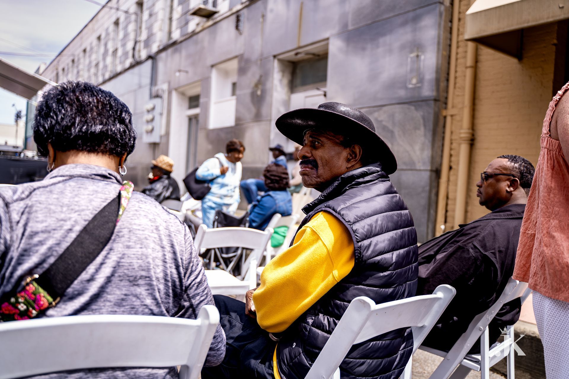 A man in a hat is sitting in a chair in front of a building.