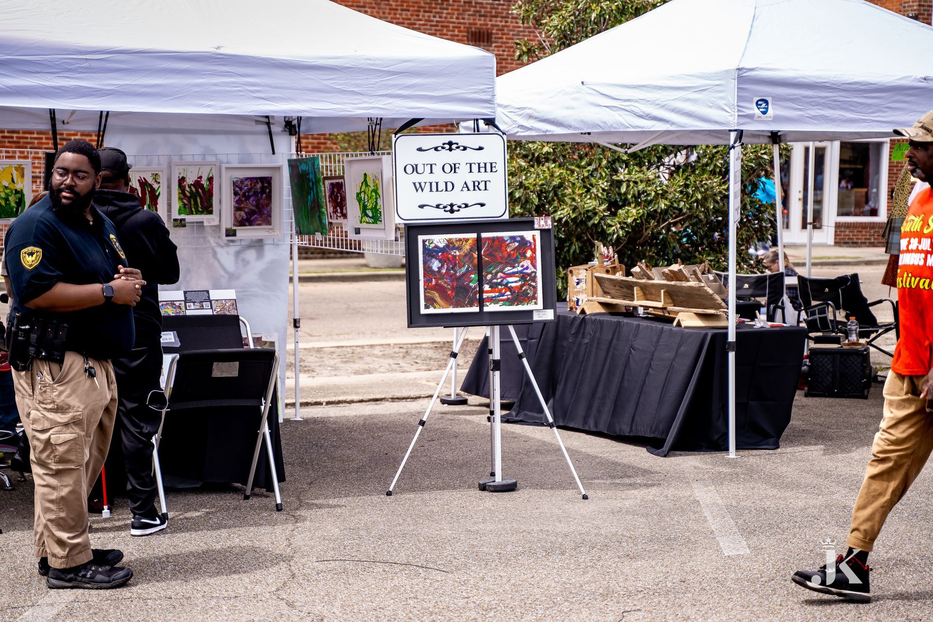 A man in a red shirt is walking past a tent with paintings on it.