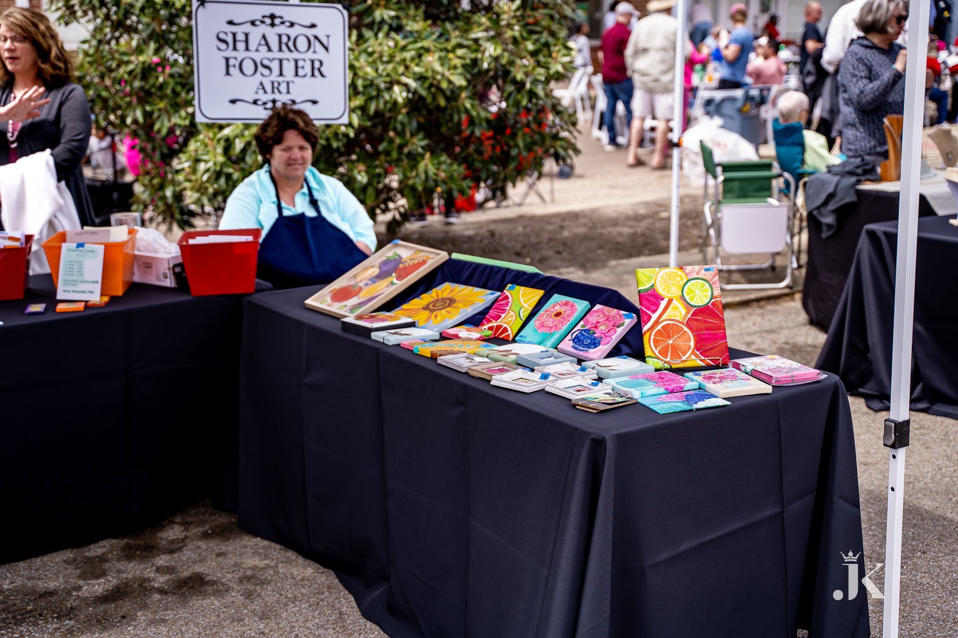 A woman sitting at a table with a sign that says sharon foster art