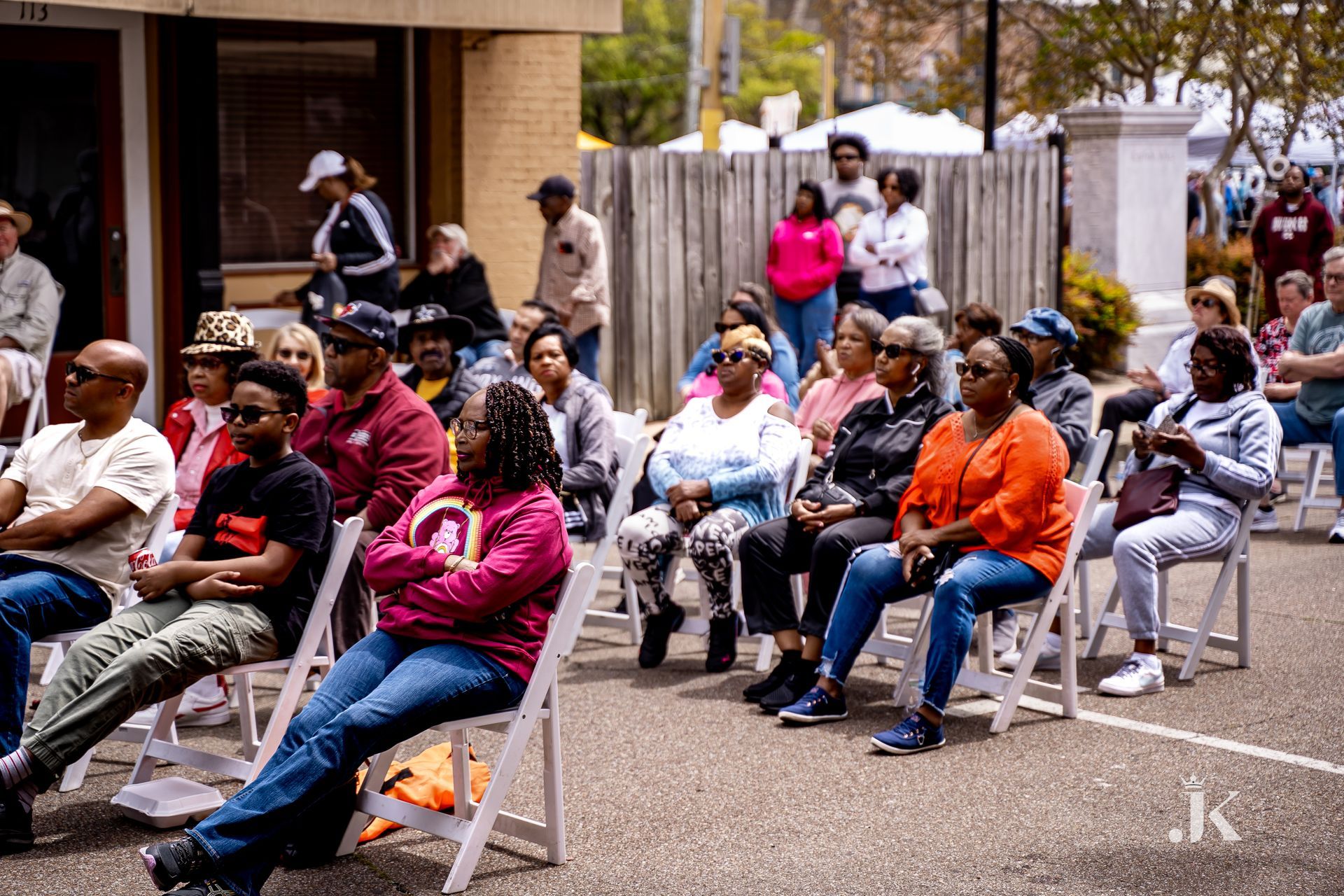 A large group of people are sitting in chairs outside of a building.