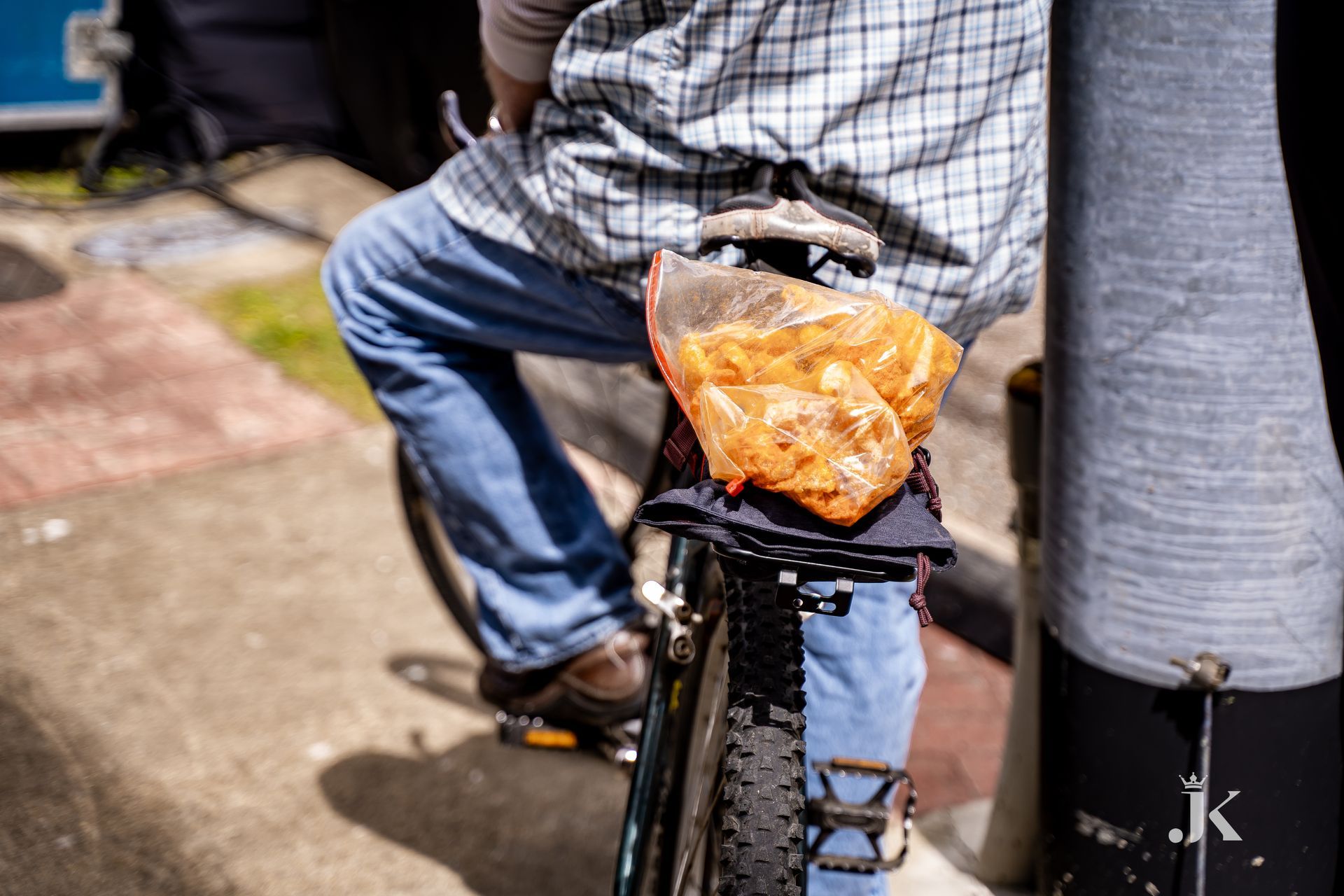A man is riding a bike with a bag of chips on the back.