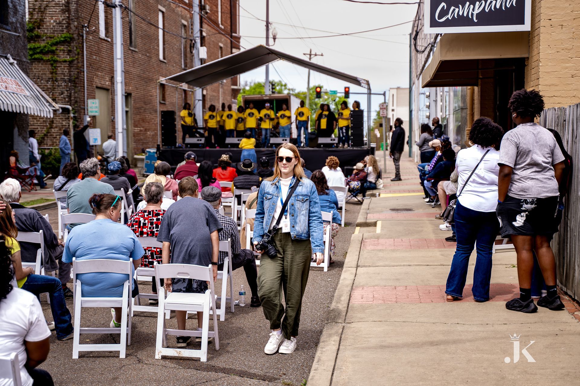 A group of people are sitting in chairs on a sidewalk in front of a stage.