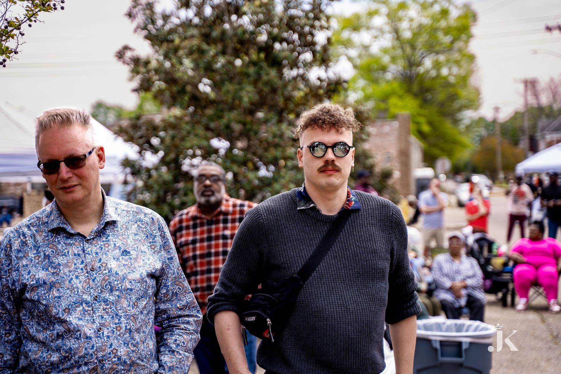 A group of men are walking down a street wearing sunglasses and mustaches.