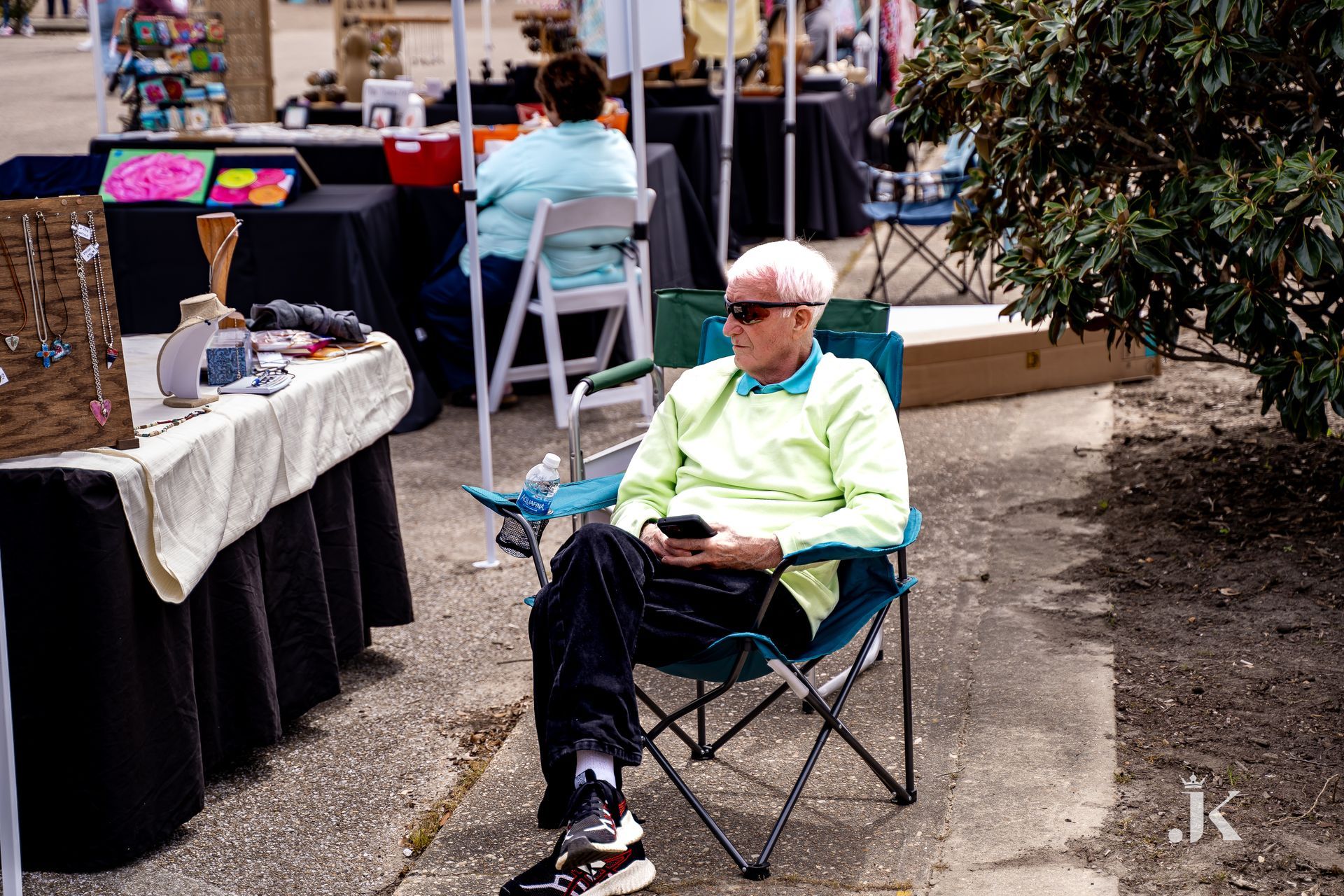 An older man is sitting in a folding chair looking at his cell phone.