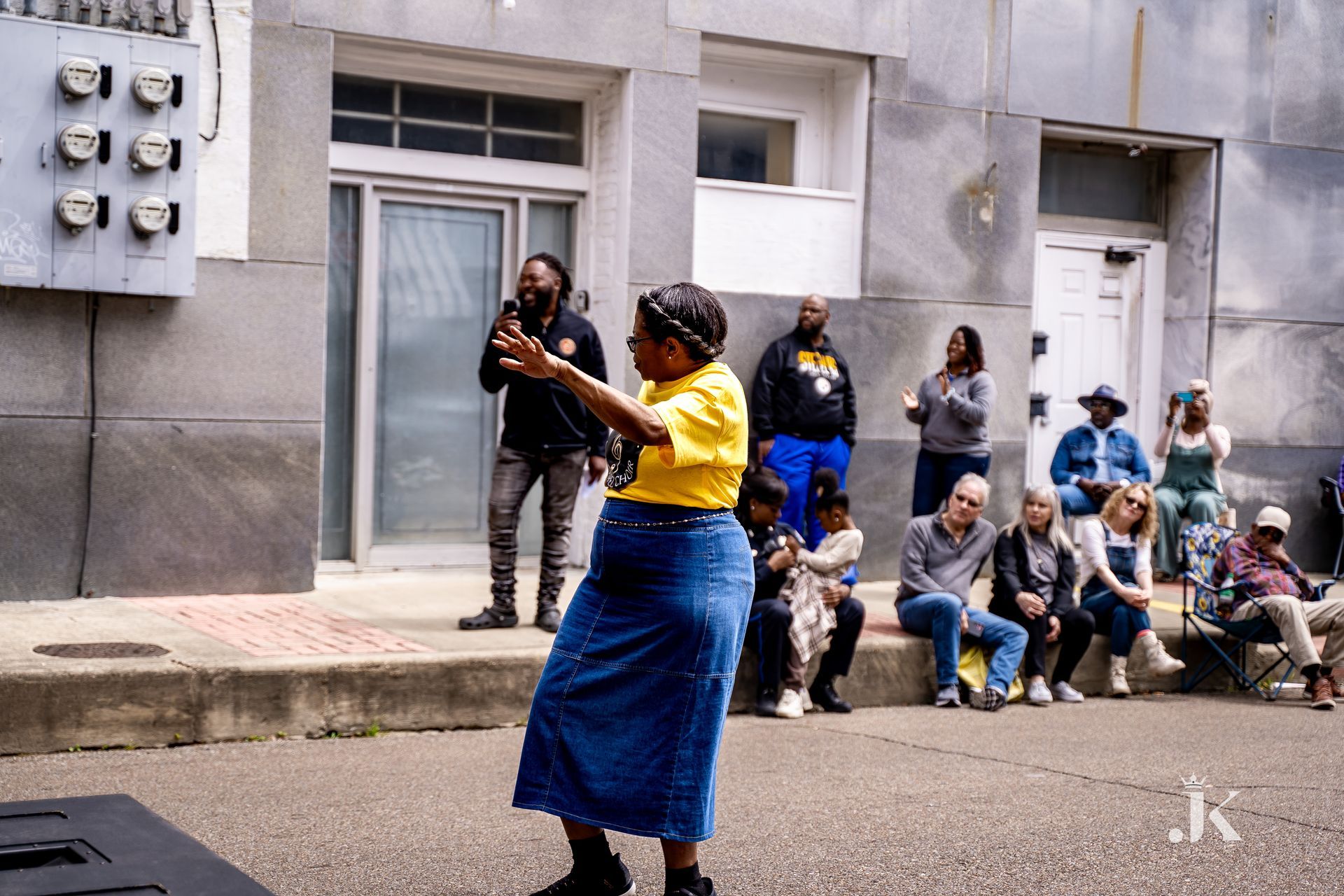 A woman in a yellow shirt and blue skirt is dancing in front of a crowd of people.
