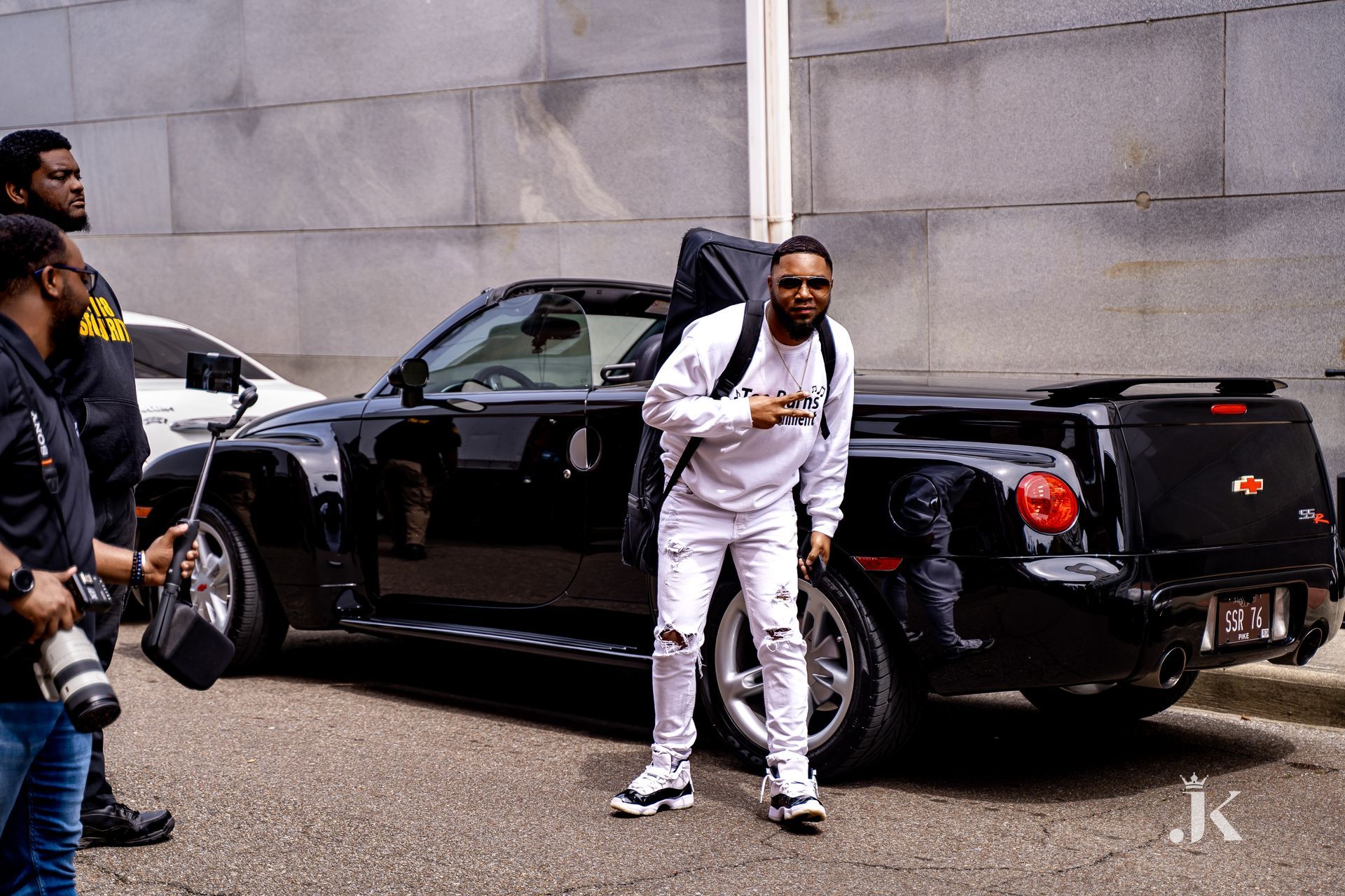 A man is standing in front of a black car.