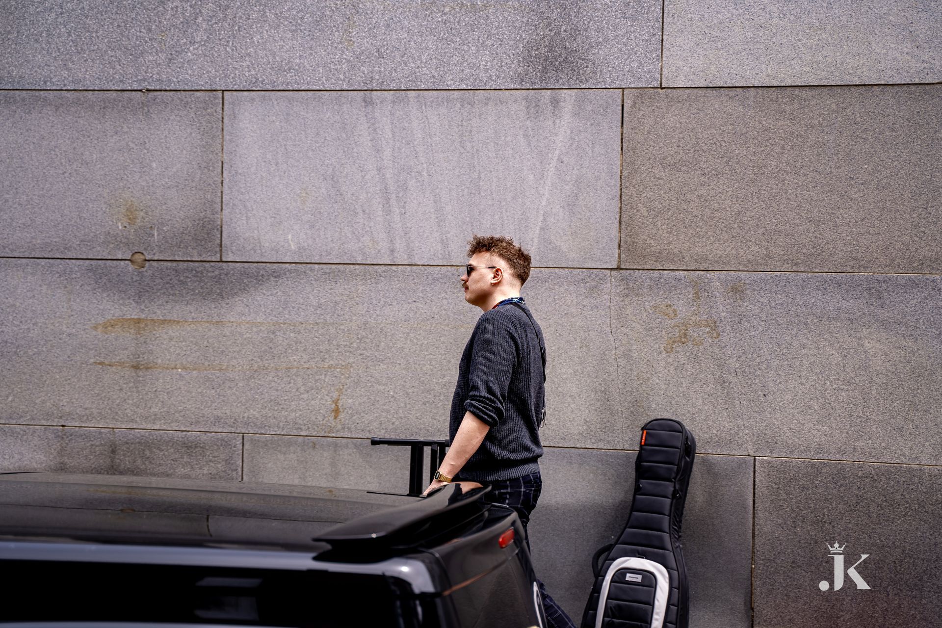 A man is standing in front of a brick wall next to a car.