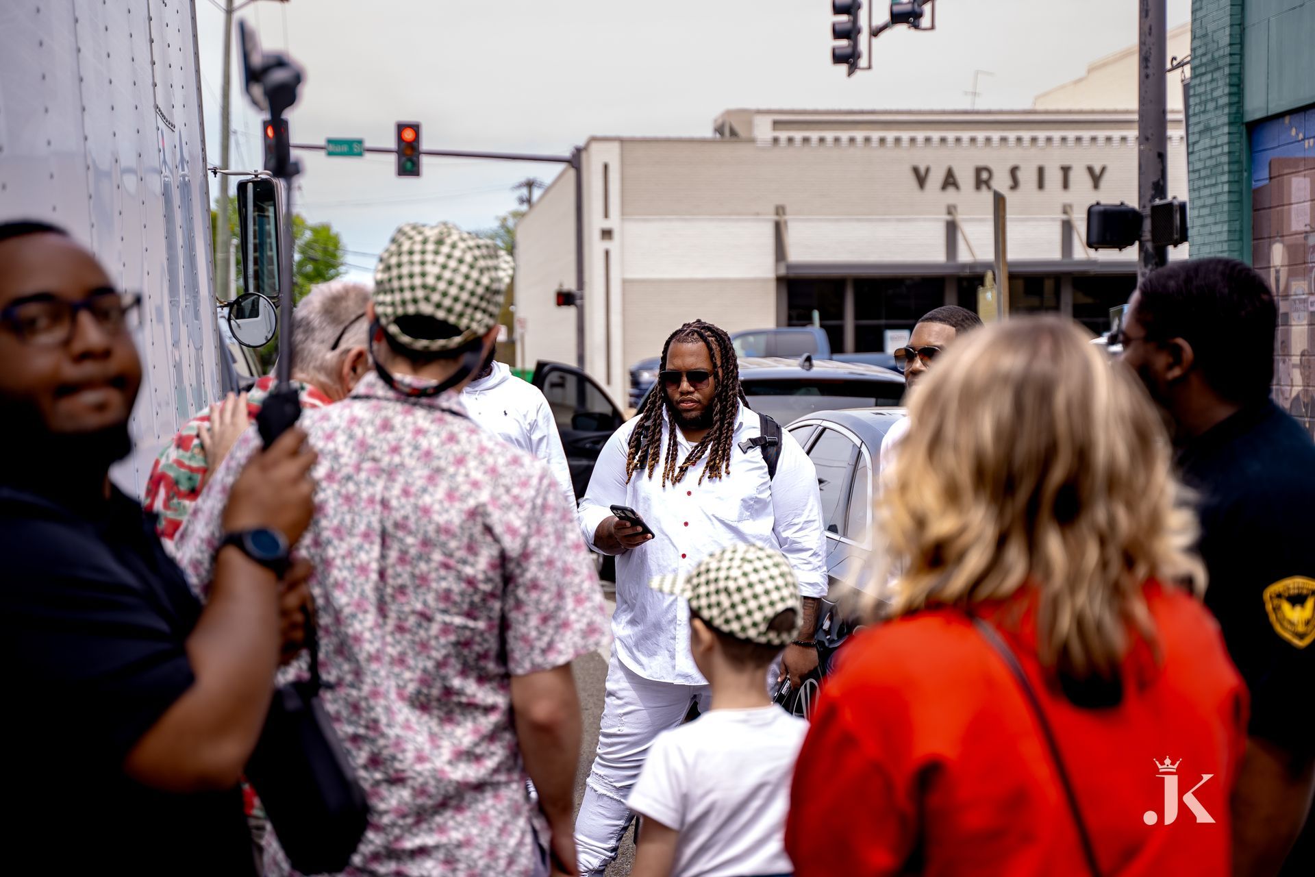A group of people are walking down a street in front of a varsity building.