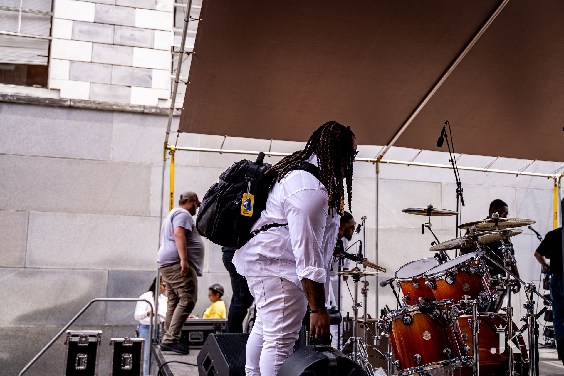 A man with dreadlocks is standing on a stage with a backpack.