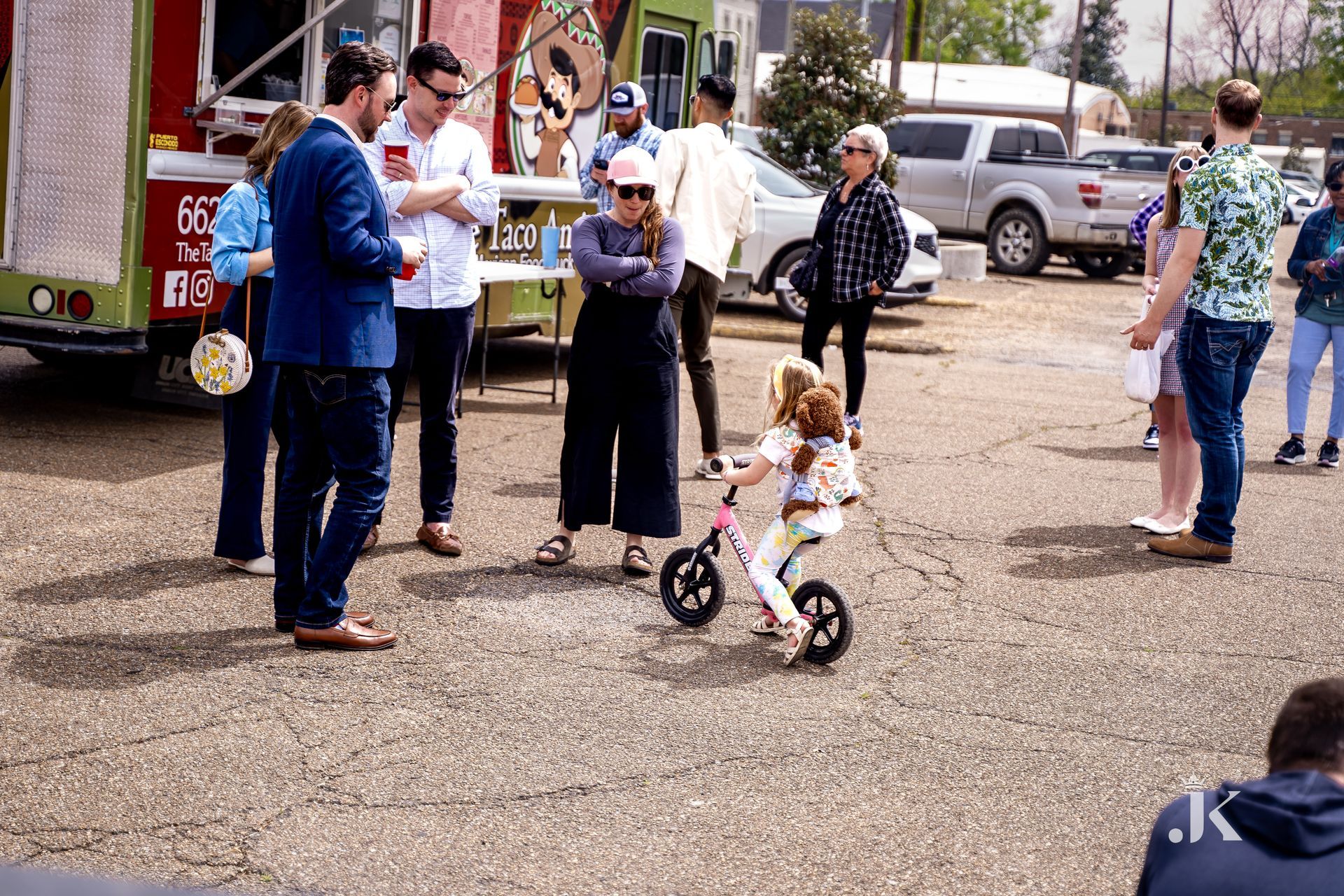 A group of people are standing around a little girl riding a bike.
