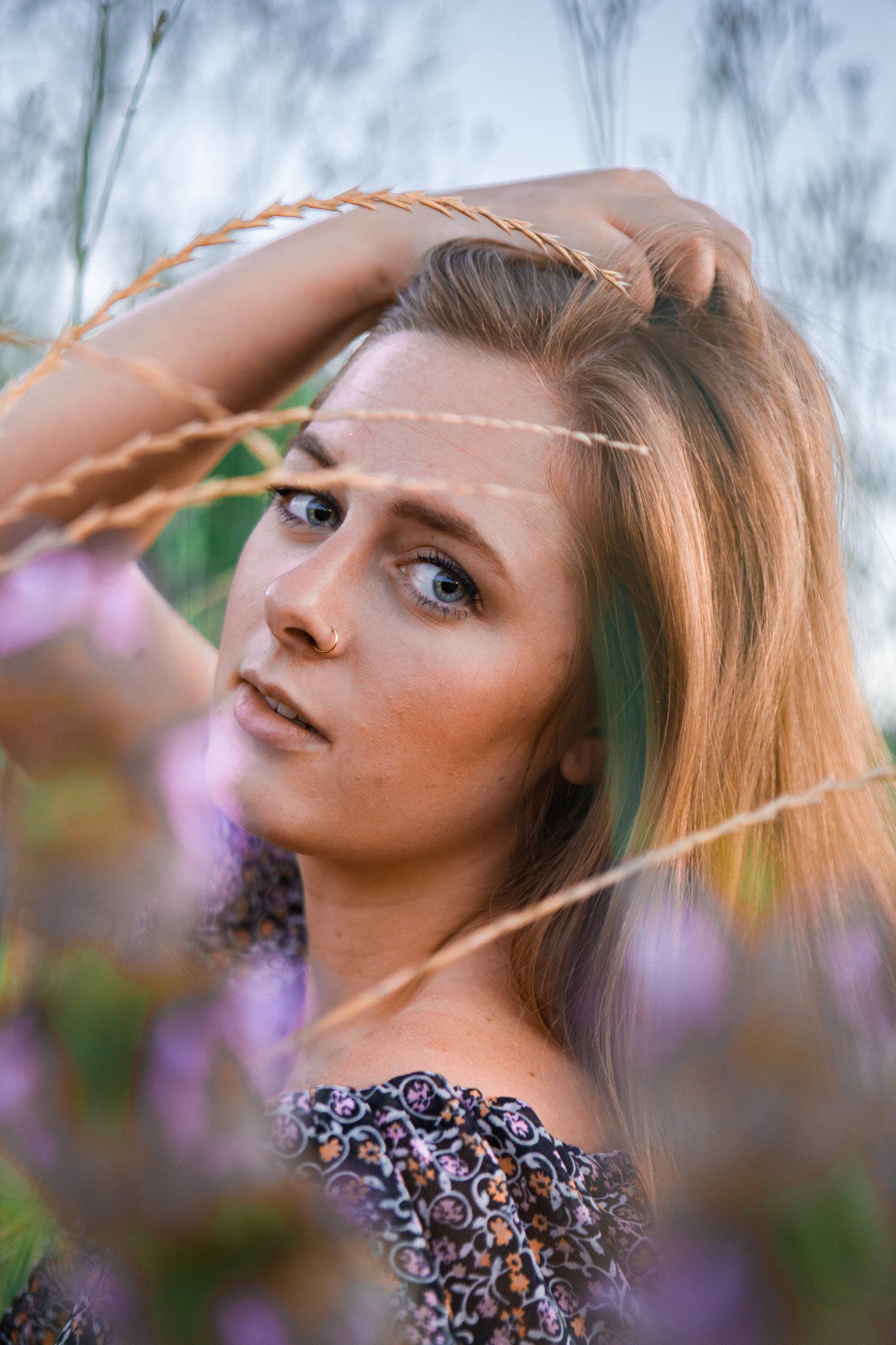 A woman is standing in a field of tall grass holding her hair.