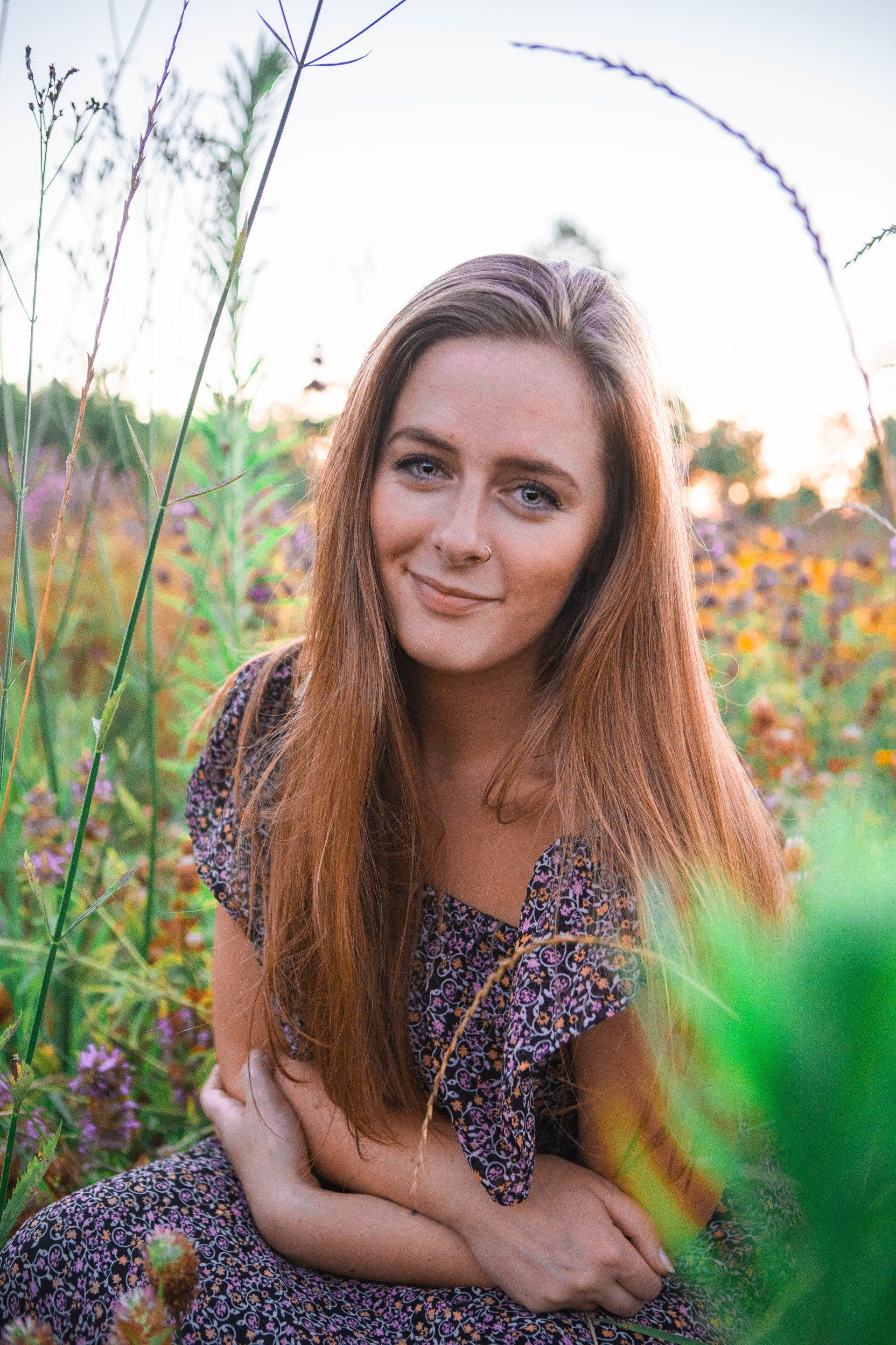 A woman in a purple dress is sitting in a field of flowers.