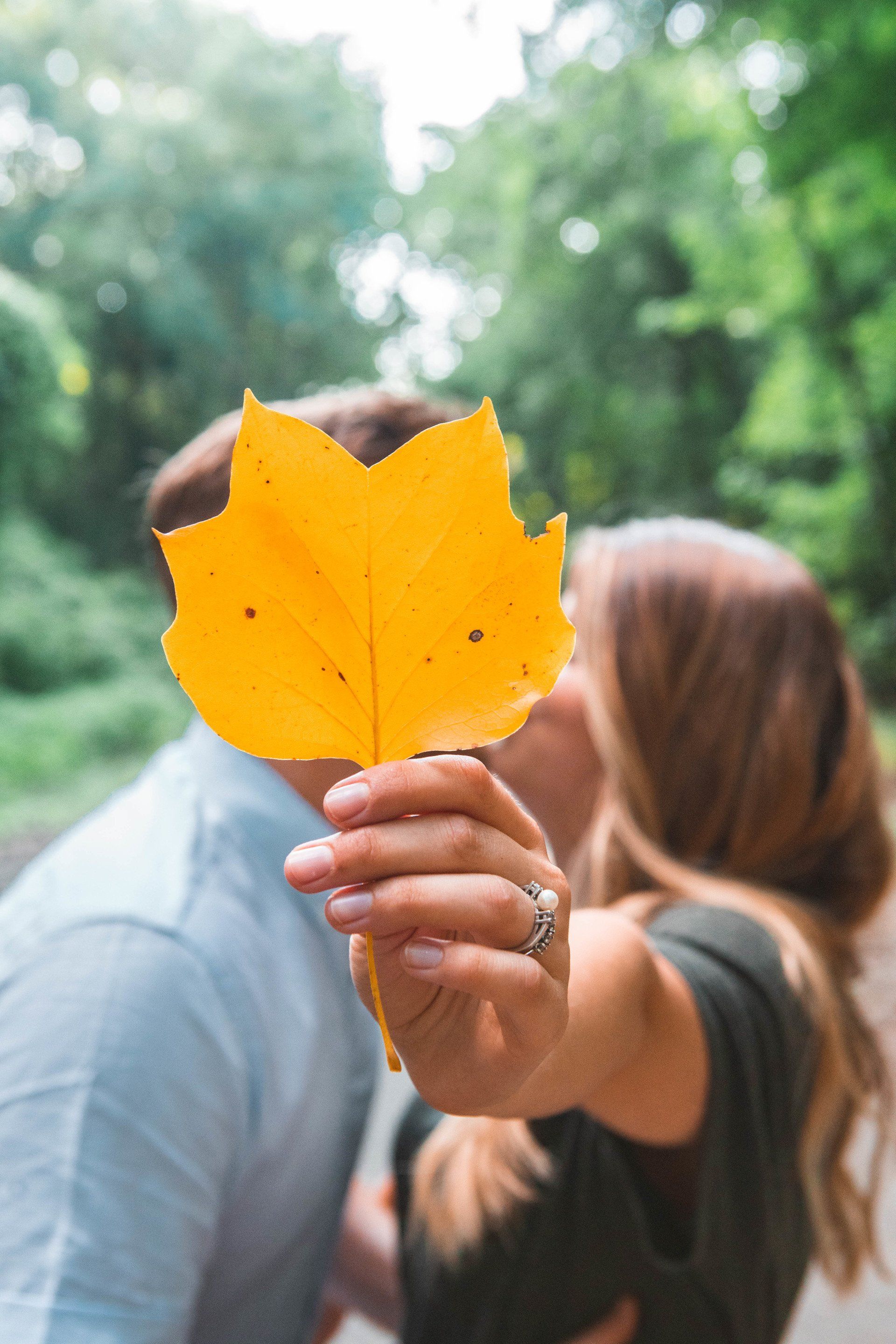 A woman is holding a yellow leaf in front of a man 's face.