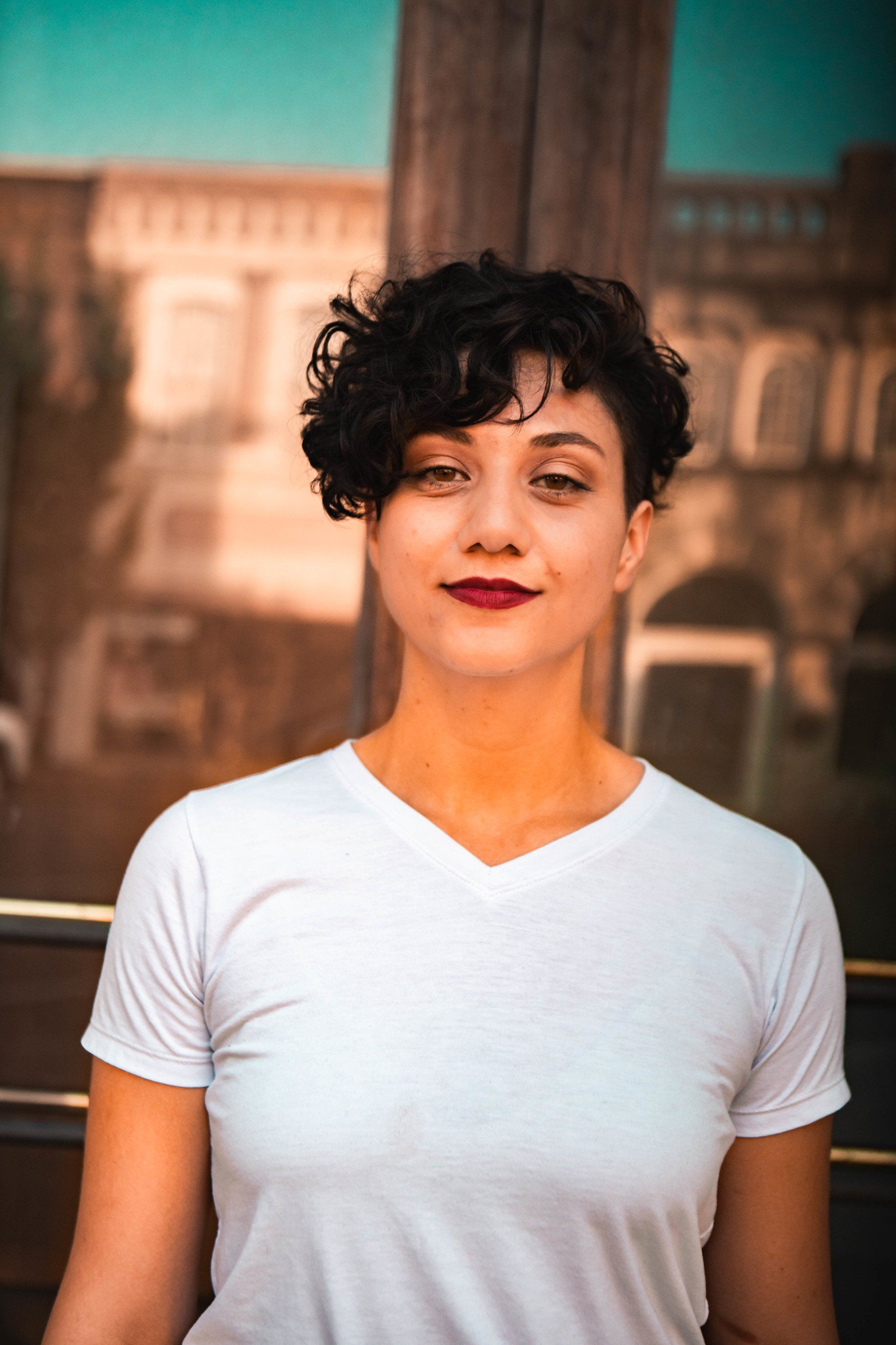 A woman with curly hair is wearing a white t-shirt and red lipstick.