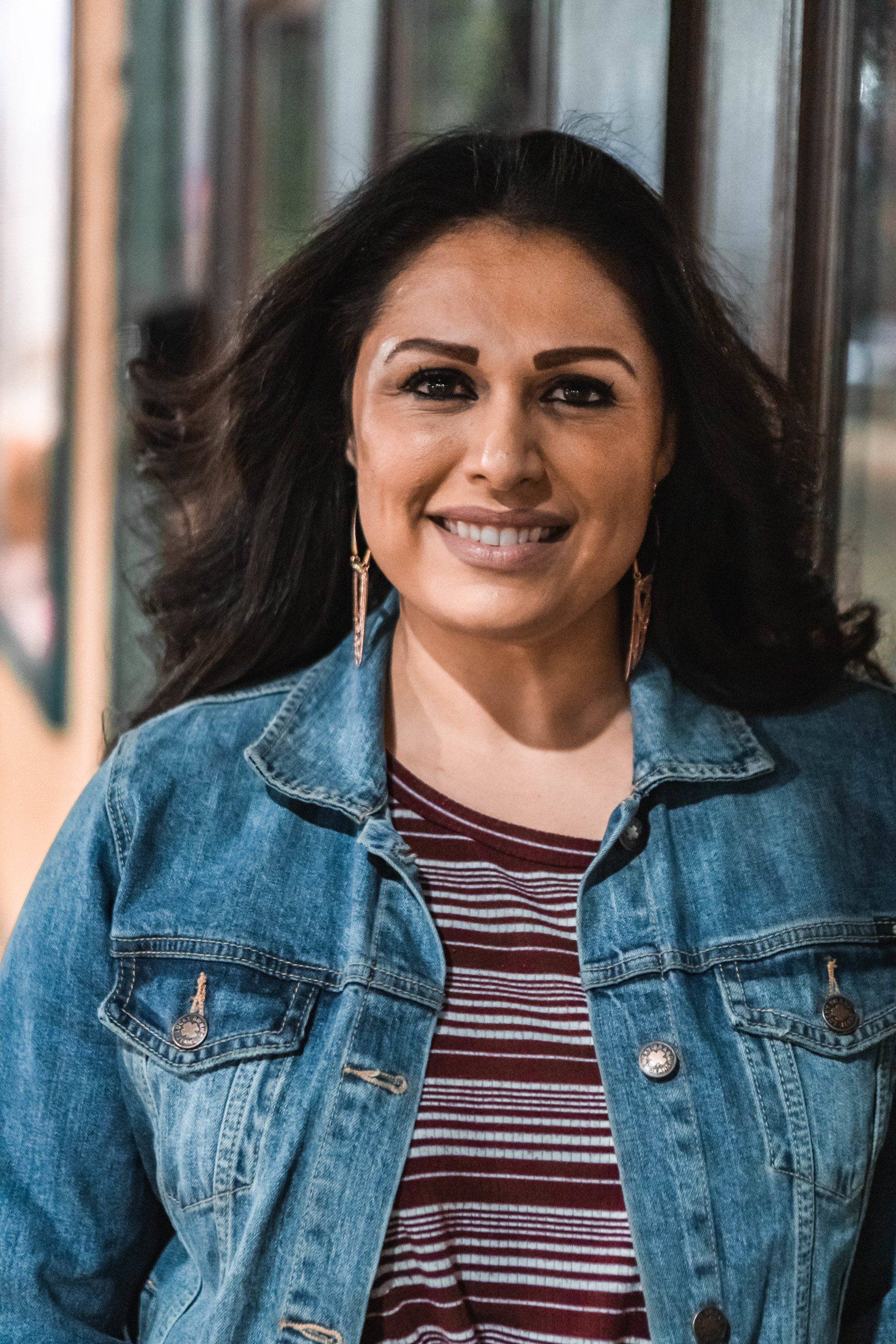 A woman wearing a denim jacket and a striped shirt is smiling for the camera.