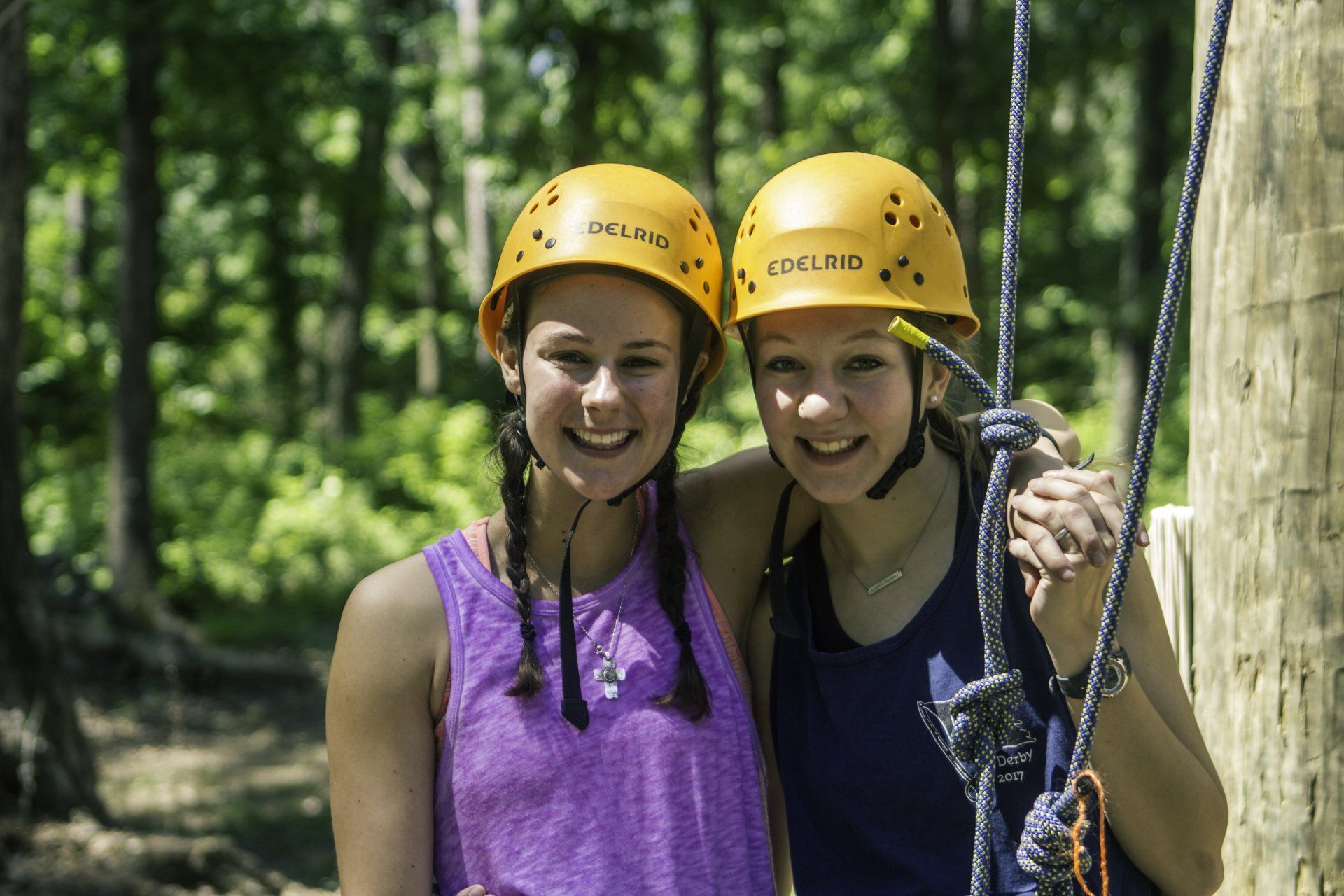 Two girls wearing helmets are posing for a picture in the woods.