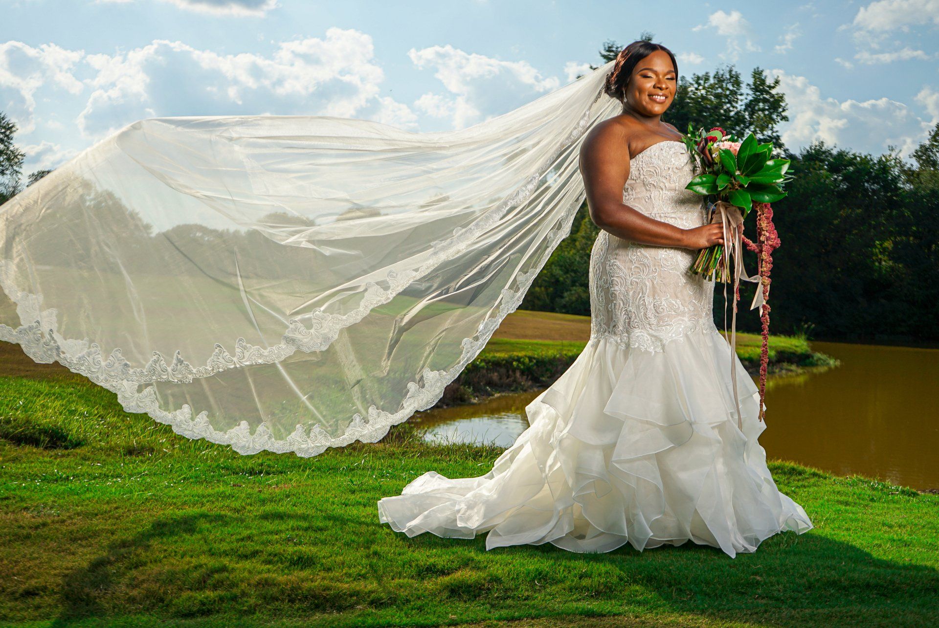 A bride in a wedding dress is standing in the grass with her veil blowing in the wind.