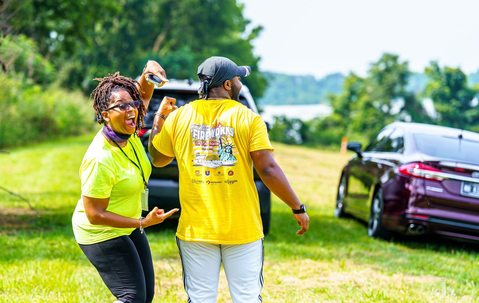 A man and a woman are dancing in a field in front of a car.