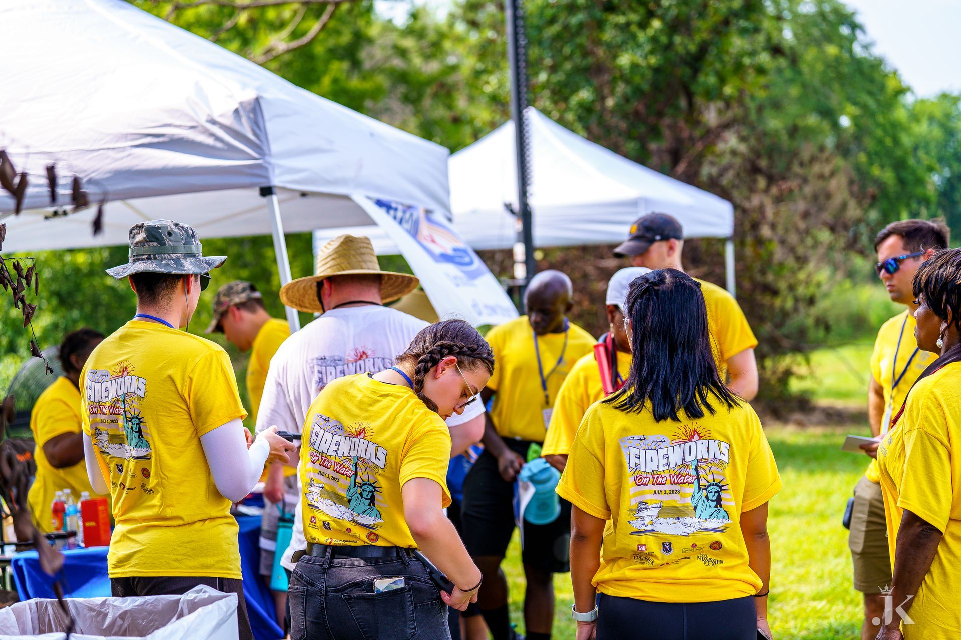 A group of people wearing yellow shirts are standing under tents in a park.