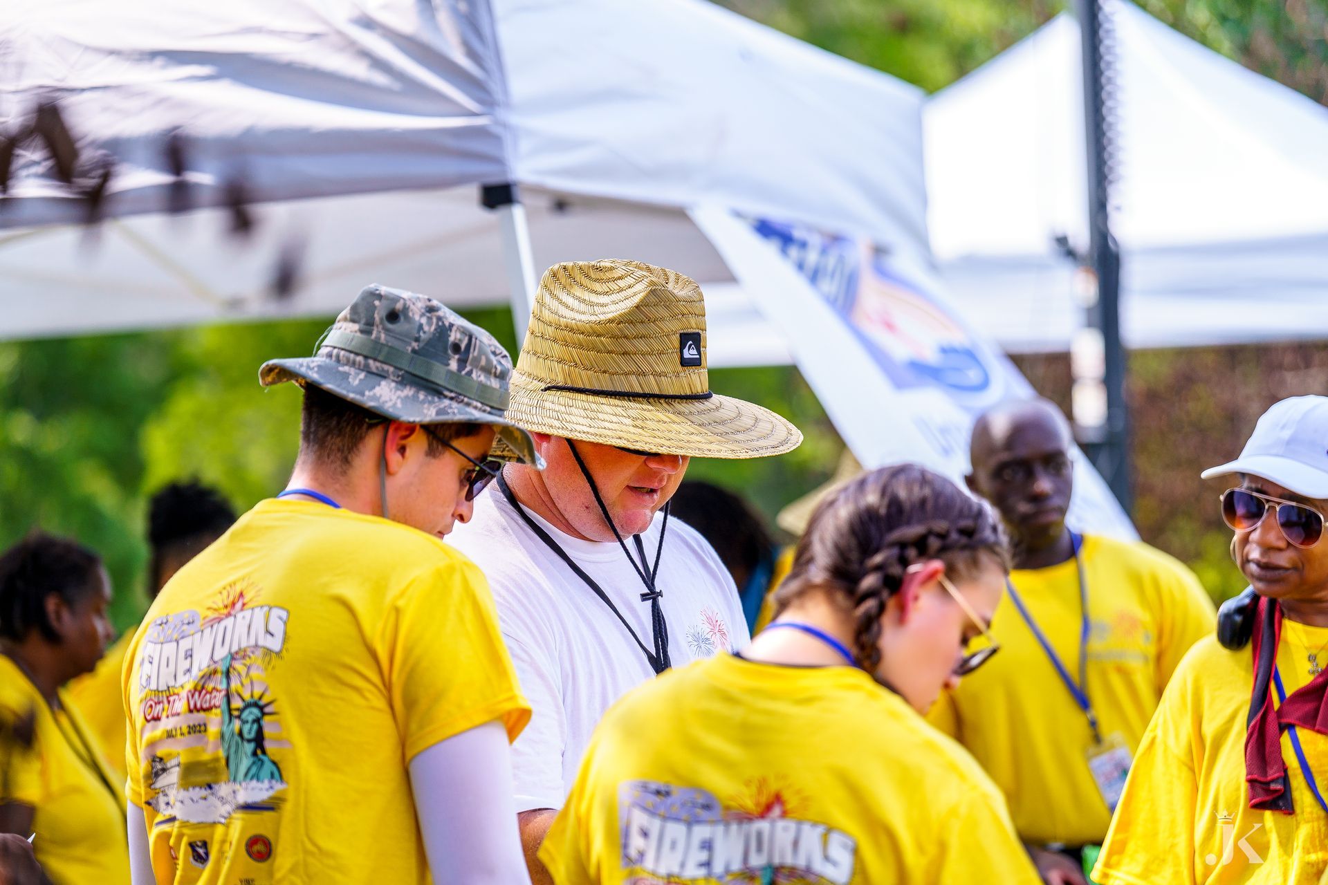 A group of people wearing yellow shirts and hats are standing under a tent.