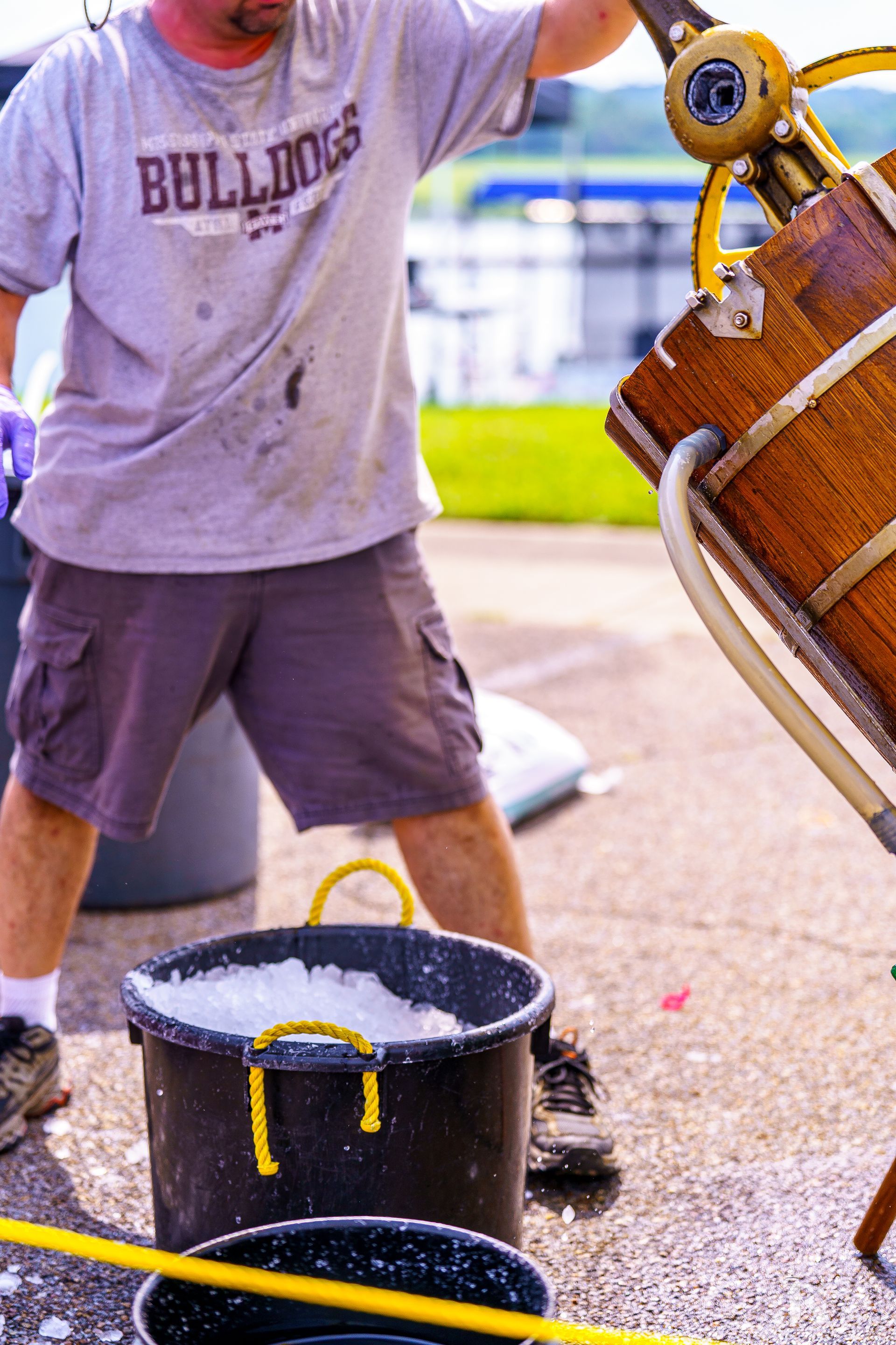 A man wearing a bulldogs shirt is pouring water into a bucket
