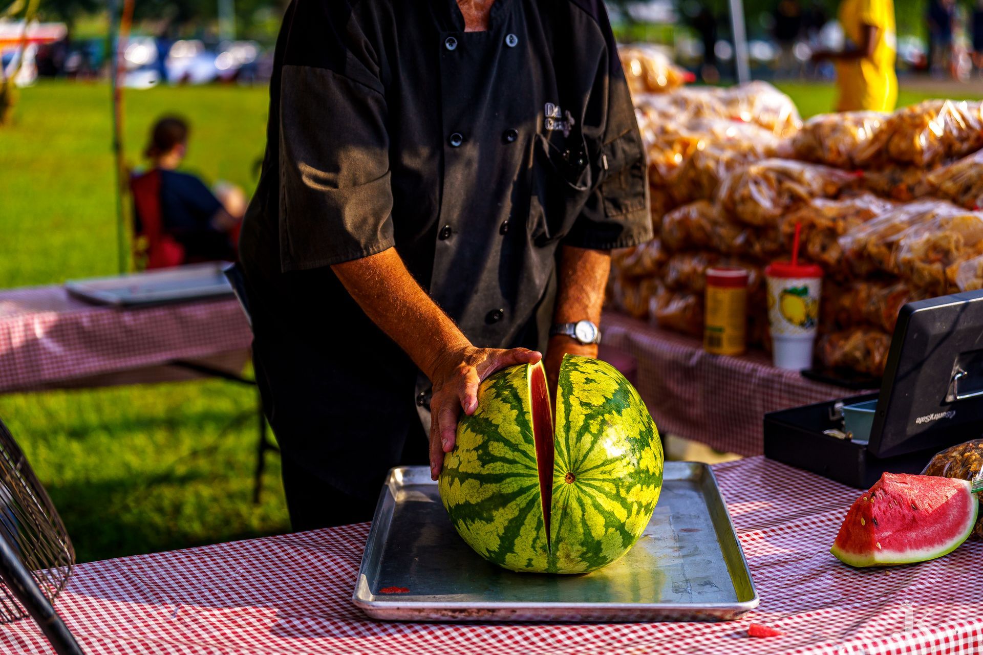 A man is cutting a watermelon on a tray on a table.