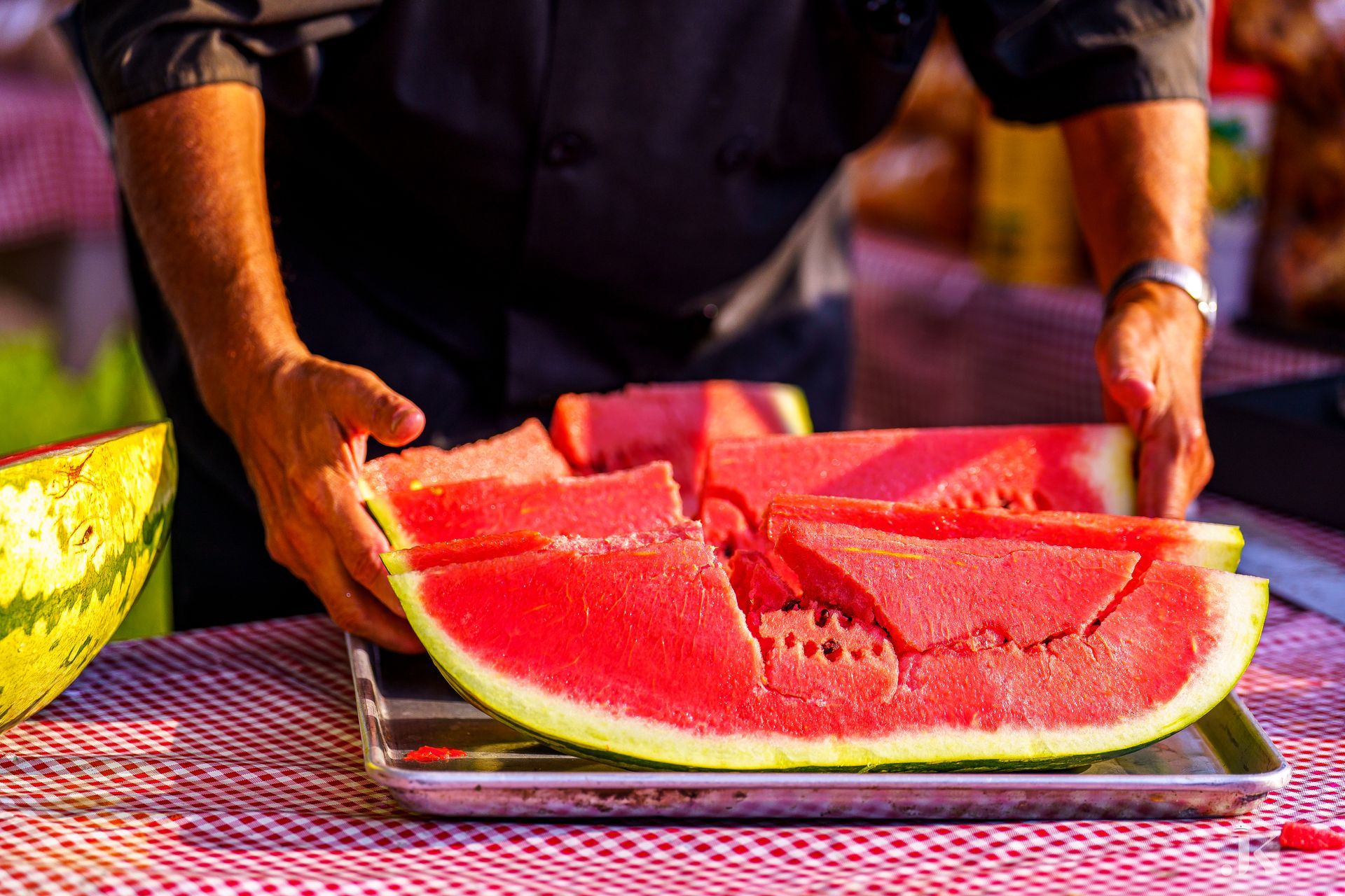 A man is cutting a watermelon into slices on a tray on a table.