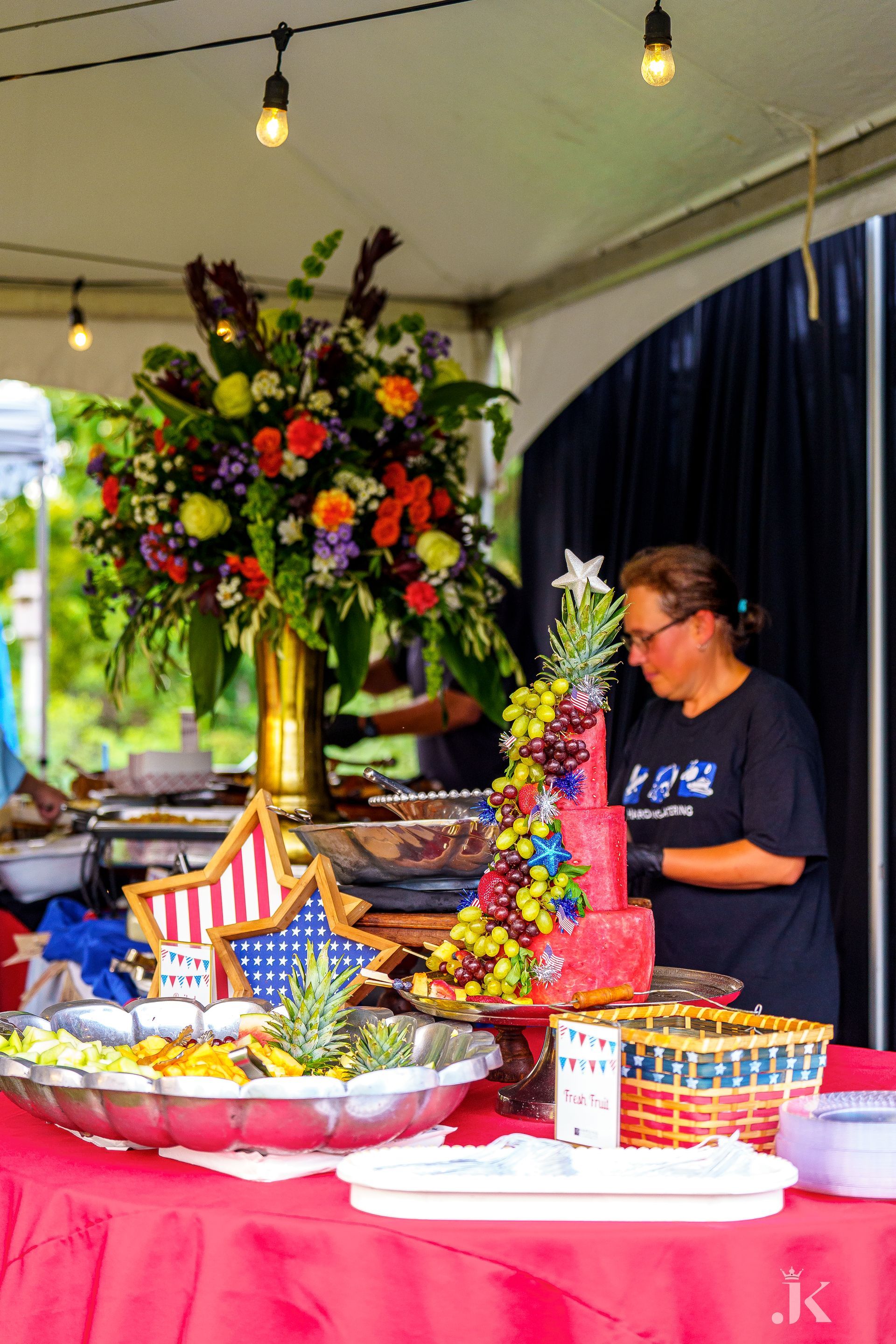 A woman is standing in front of a buffet table with fruit and flowers on it.